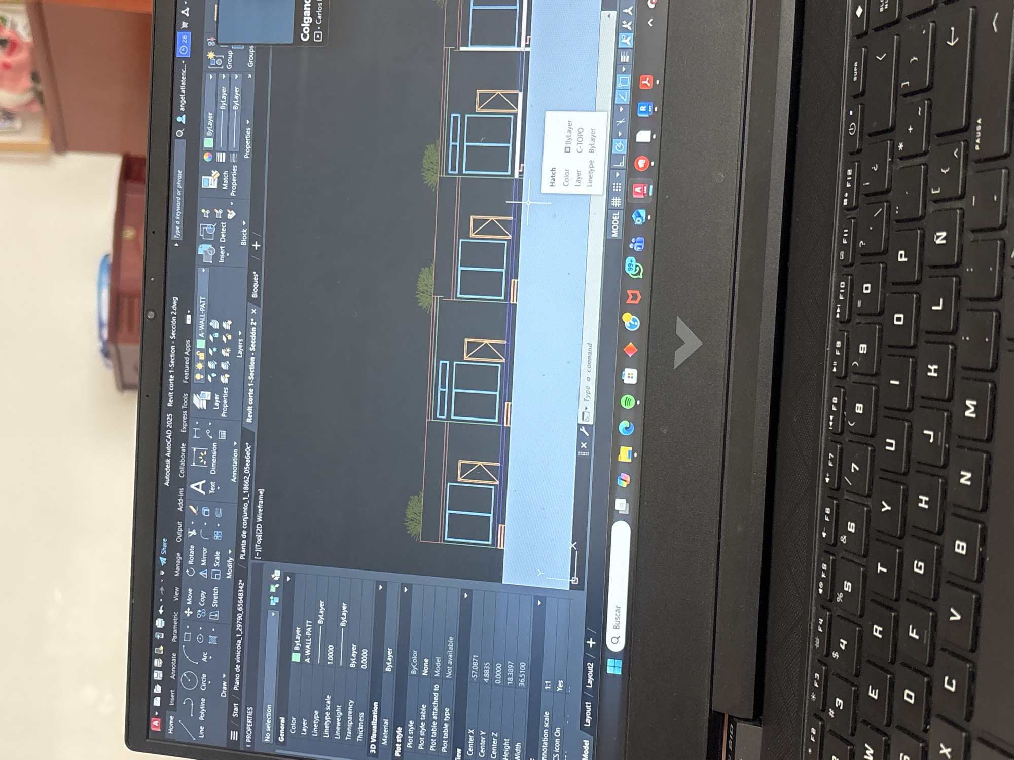 Here's a detailed description of the image:
**Scene:** A close-up shot of a laptop screen displaying an AutoCAD 2025 interface with a 2D architectural drawing. The drawing shows a series of adjacent structures or buildings.
**Details:**
* **Software:** Autodesk AutoCAD 2025.
* **File Names:** "Revit corte 1-Section - Sección 2.dwg" and "Planta de conjunto_1_18662_05ea6e0c."
* **Drawing Content:** The architectural drawing shows a series of repeating units, possibly sections of a building. Elements include walls, windows, and some landscaping details (e.g., shrubbery). The pop-up suggests that the layer for 'C-TOPO' which is most likely contour lines, is visible.
* **Properties Panel:** A properties panel on the left side of the screen indicates parameters for selected objects (or lack thereof), including color, layer, linetype, scale, and other attributes.
* **Keyboard:** Part of the laptop keyboard is visible on the right.
**Environmental and Contextual Notes:**
* The language setting on the keyboard is Spanish, which is consistent with the software menus, file names, and search bar in the bottom right that says "Buscar."
**Location Inference:**
* Given the presence of the Spanish language settings and references to "vinicola" (vineyard), it's reasonable to assume the drawing pertains to a project in a Spanish-speaking country. San Pablo del Monte is in Mexico, where Spanish is spoken. However, without specific details on the design itself, it's impossible to definitively confirm San Pablo del Monte as the location.