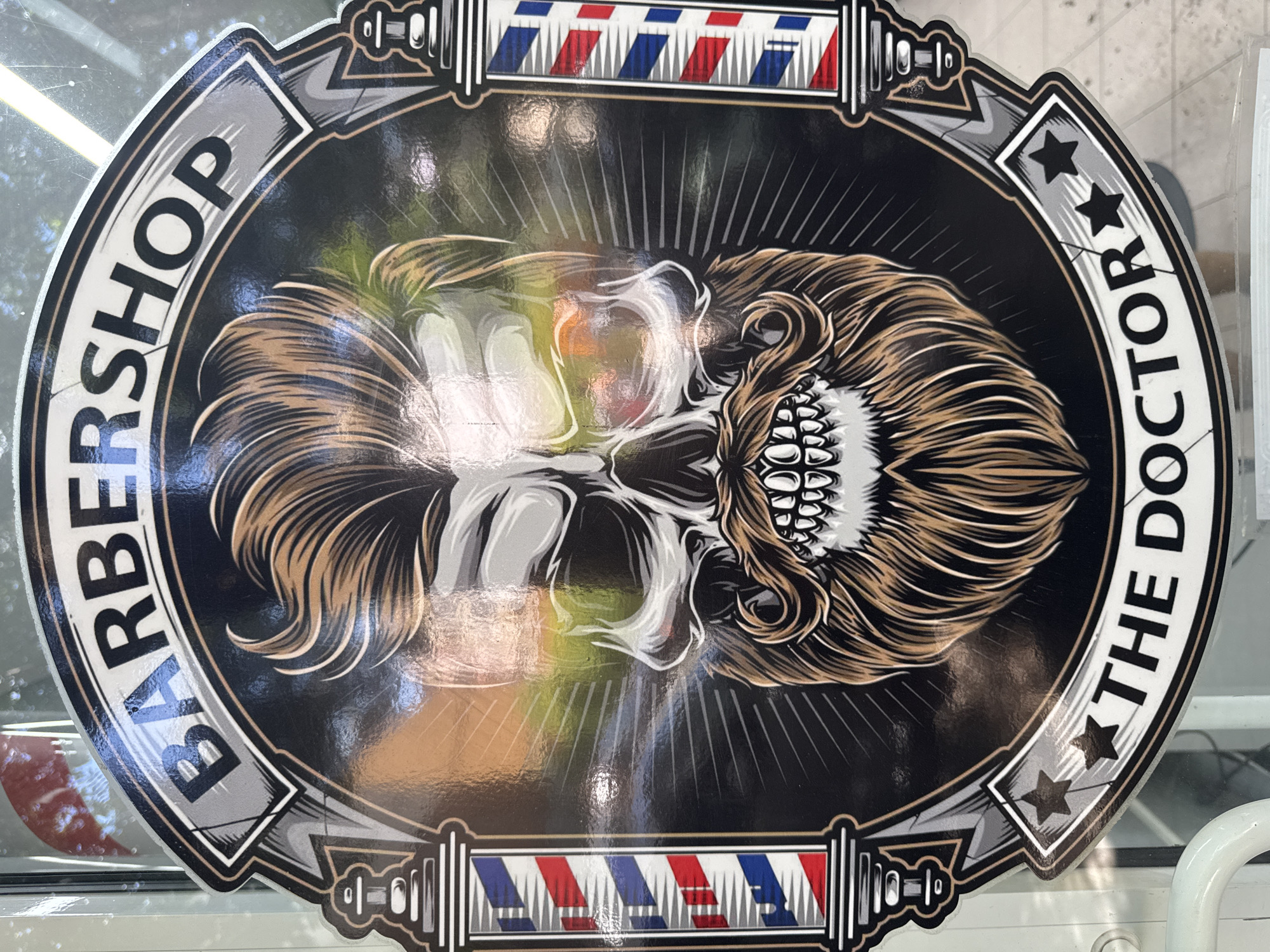 The image shows a Barber Shop logo. The logo is oval-shaped, featuring a skull with stylized hair. The text "BARBERSHOP" is on the left side of the oval and "THE DOCTOR" on the right side, each with a star. Barber pole images are located at the top and bottom of the logo. The city and state of the location are unknown.