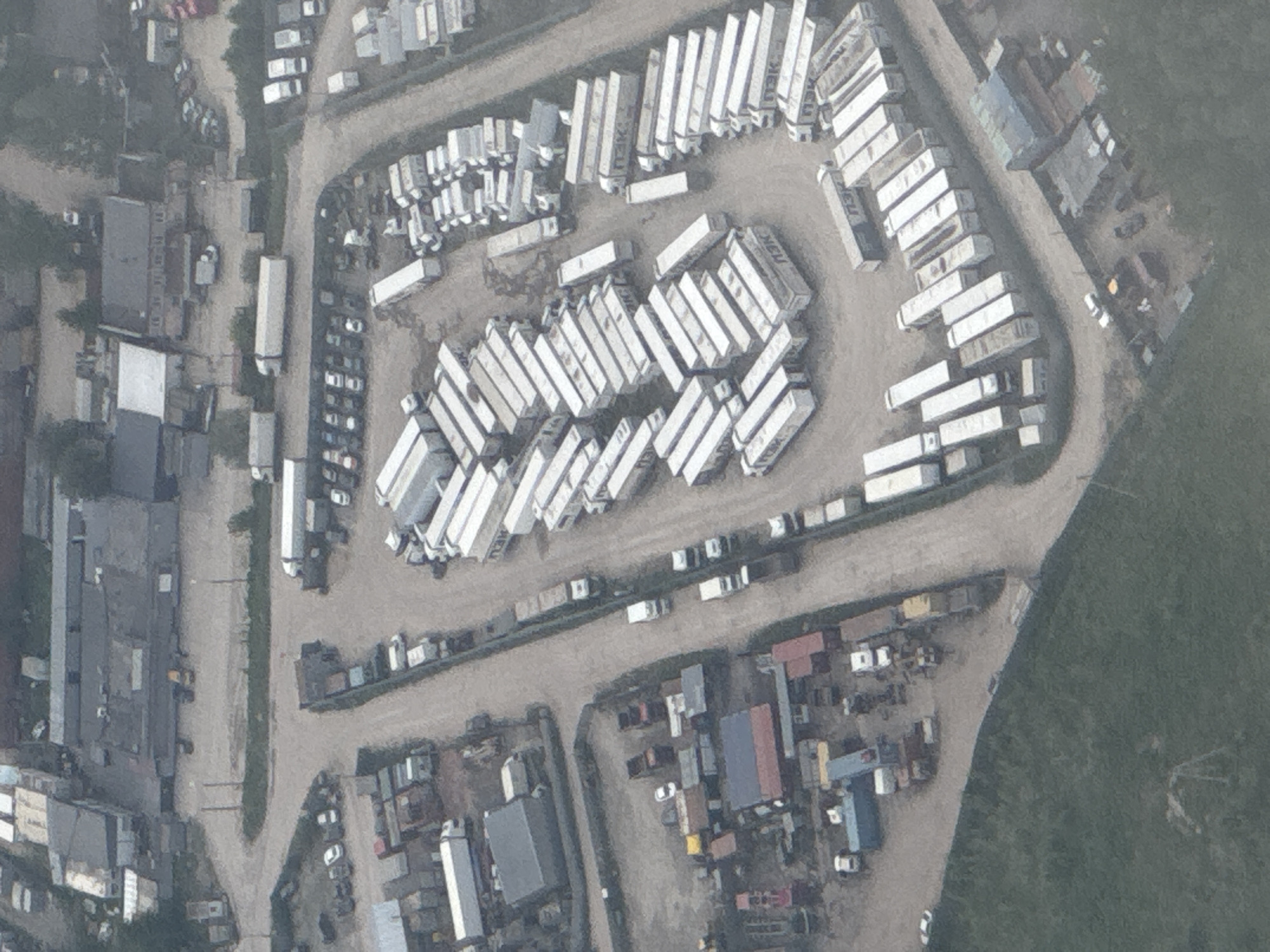 Aerial view of an industrial area in Khimki, Russia. Dominated by rows of white semi-trailer containers. Gravel roads and yards with buildings and materials. Green field adjacent to the industrial zone.