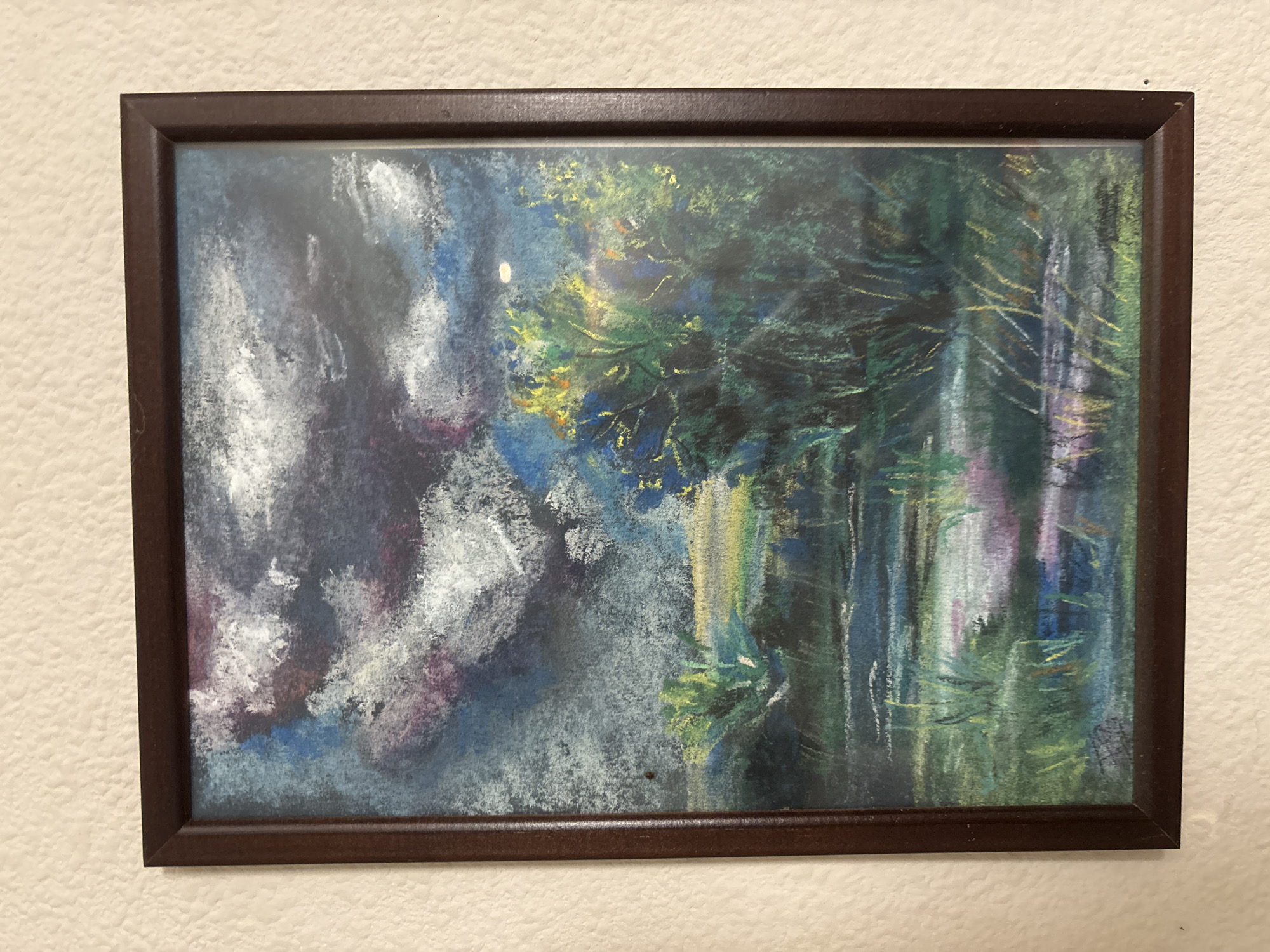 The image shows a framed pastel drawing of a landscape. The drawing depicts a dark, cloudy sky with hints of blue and purple, above a scene of marshy land with water and vegetation. Tall reeds and grasses are visible along the water's edge, and a cluster of trees with yellow and green foliage is prominent on the right side of the drawing. The water reflects the colors of the sky and surrounding landscape. The drawing is framed in a dark brown wooden frame and hangs on a textured, off-white wall. The location of Svkh Maslovskiy 1 Otdeleniye, Russia, is not depicted in the image.
