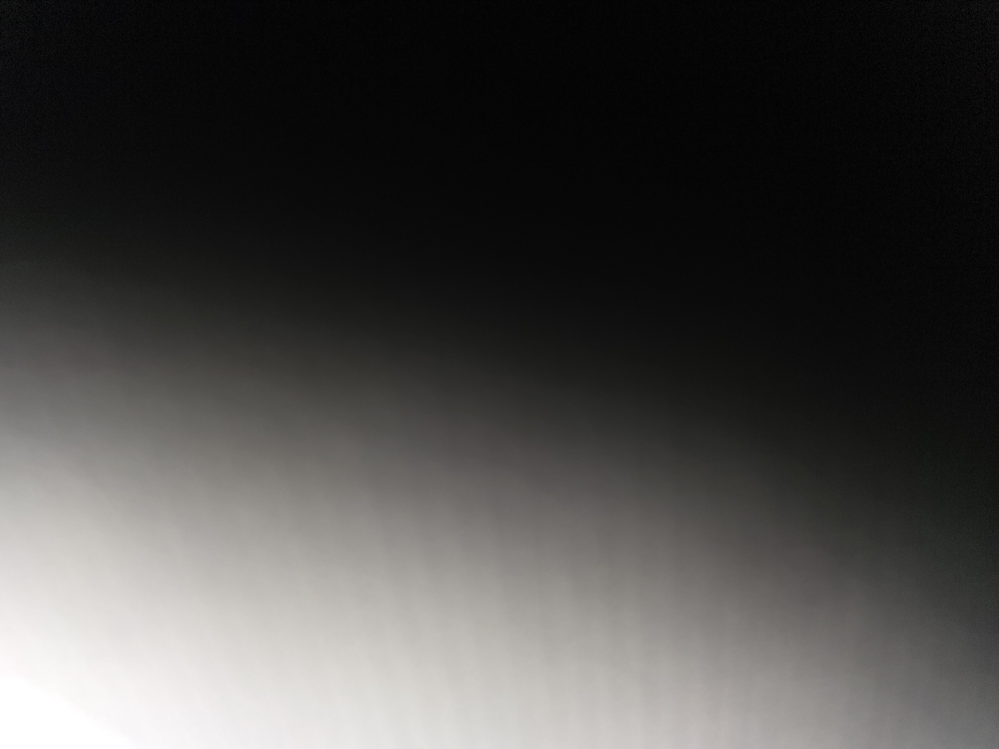 The image is a photograph with a gradient of light and dark, transitioning from bright white in the upper left corner to black in the lower right corner. There are subtle horizontal lines visible, suggesting a textured surface, possibly fabric or a screen, that is illuminated from the left. The image is abstract and does not depict any recognizable objects, people, or a specific location within the city of Ulan-Ude, Russia.