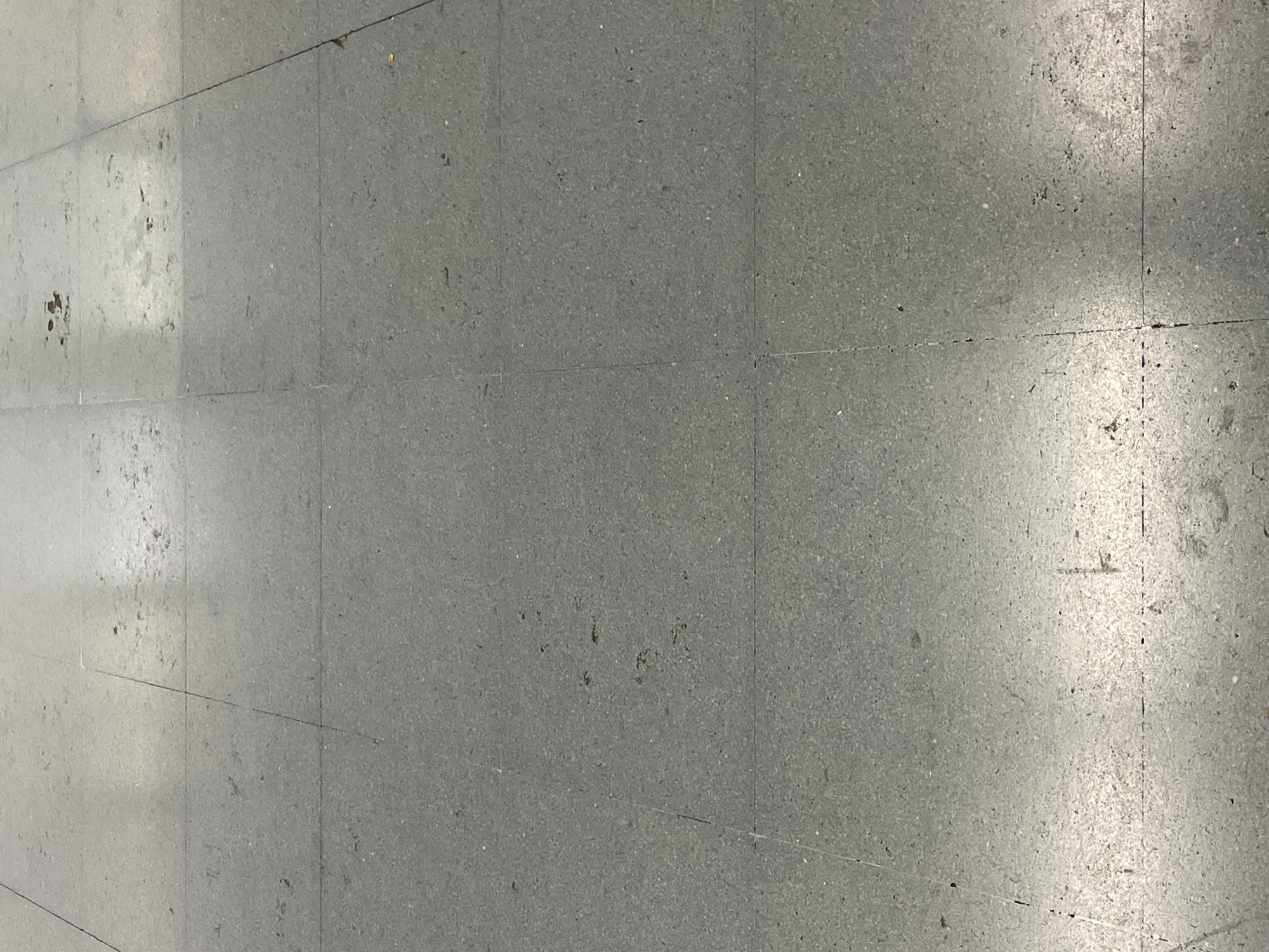 The image shows a gray tiled floor. The tiles appear to be square or rectangular and are laid out in a grid pattern with dark lines marking the seams. The floor appears to be slightly worn and dirty with dark spots and patches of discoloration. There is no indication of a specific location in València, Spain. There are no people or objects of interest shown in the image.