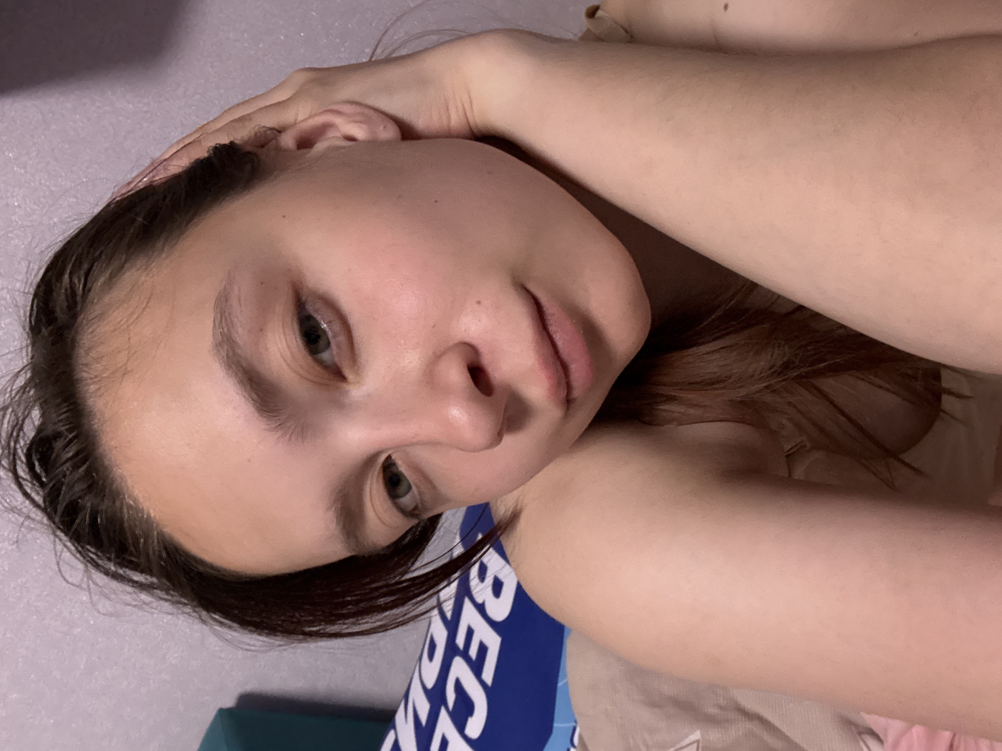 A young woman is lying down with her head resting on her hand. She has fair skin, brown hair, and green eyes. The background is a wall and part of a pillow. Based on the information provided, it is presumed that the location is in the city of Прикамский, Russia.