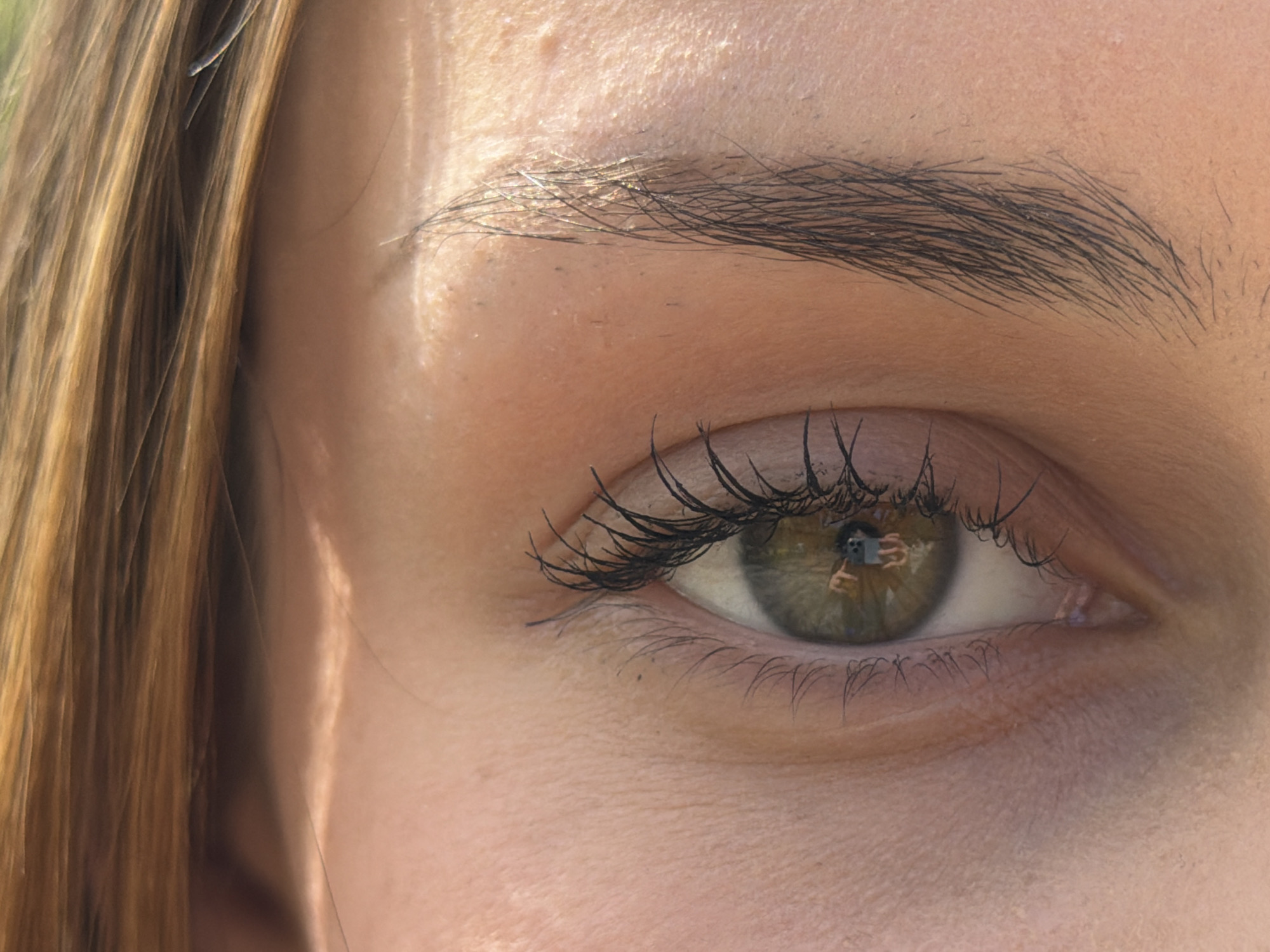 A close-up photograph showcases a person's right eye. The eye is green, with a reflection visible within the pupil showing a person holding a camera. The person has fair skin. The eyebrow is dark and well-defined. Eyelashes are visible on both the upper and lower eyelids. Part of the face is visible, including the cheek and forehead. To the left, there is a section of light brown hair. The location in Sofia, Bulgaria is not evident from the image.