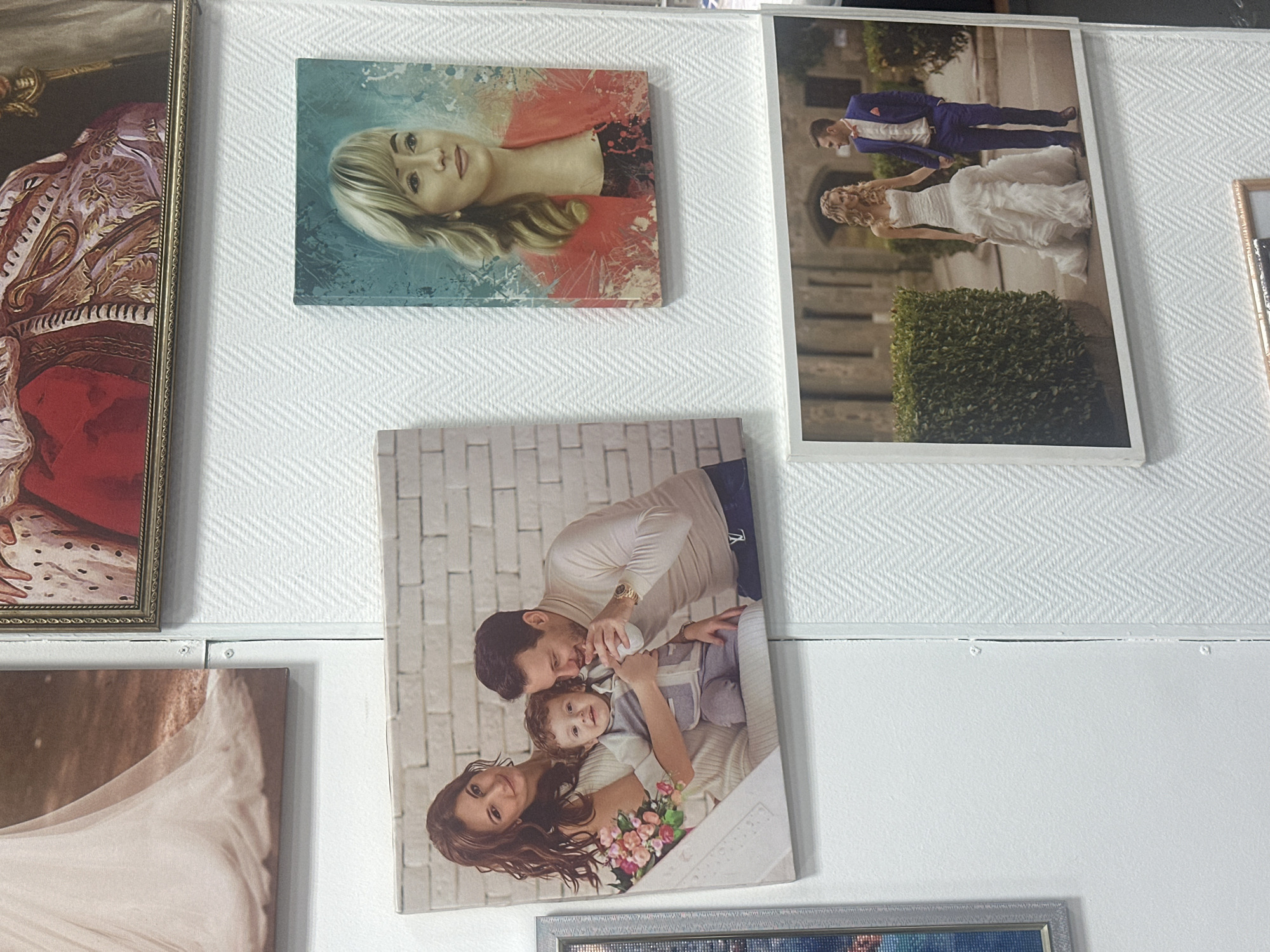The image displays a collection of framed photographs mounted on a white, textured wall. The photographs feature various subjects, including a family, a portrait of a woman, and a wedding couple. The lighting suggests an indoor setting, possibly a home or a gallery. The overall impression is one of personal memorabilia or display art. The location in Novoaltaysk, Russia is not discernible from the visual content of the image.