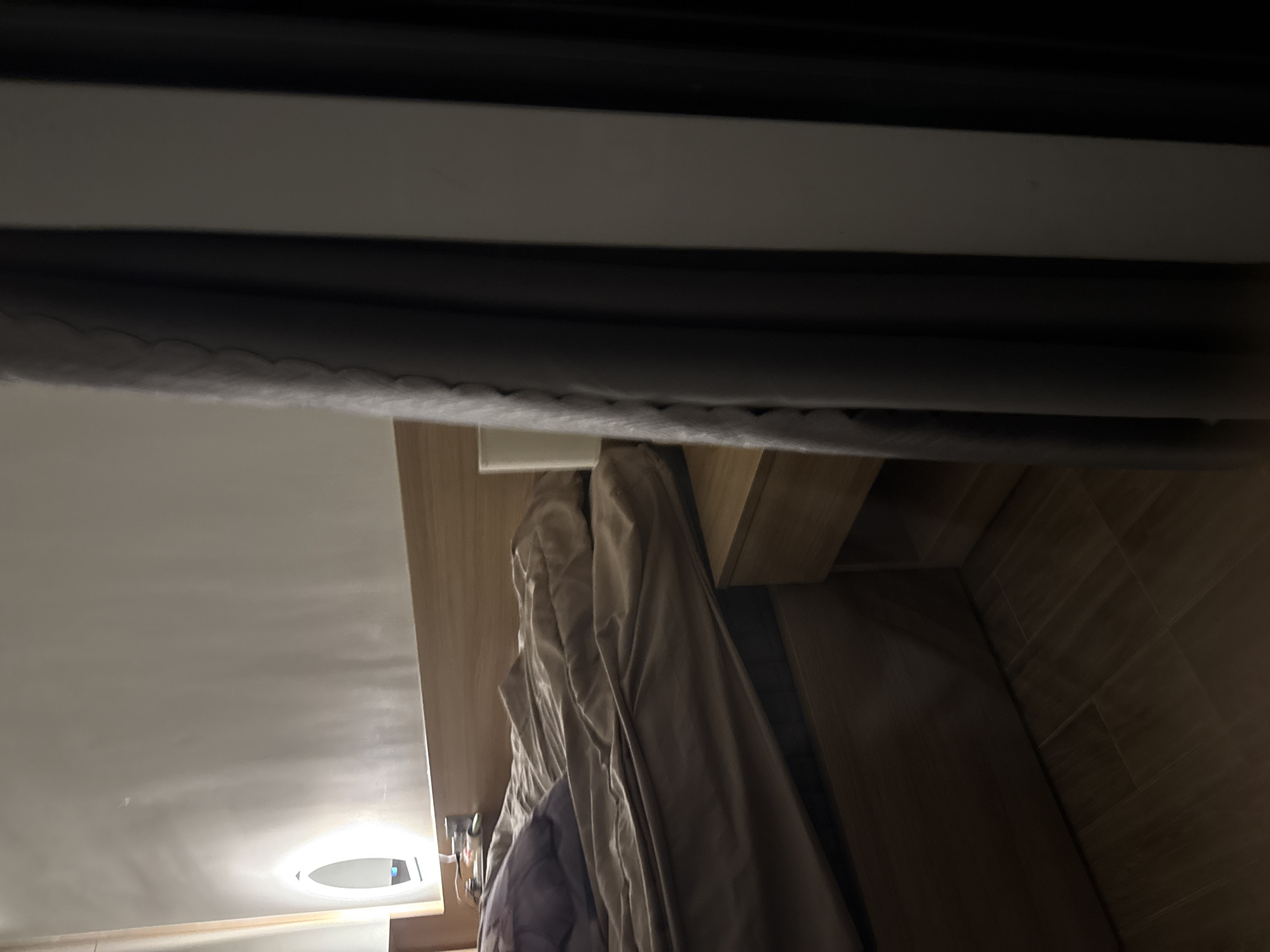 The image shows the interior of a closet. Within the closet hangs a brown jacket. The closet is constructed of wood and has a light fixture on the ceiling of the room. The closet is likely located in a residence, but it is not possible to determine if it is in the city of Đà Nẵng, Vietnam from the image.