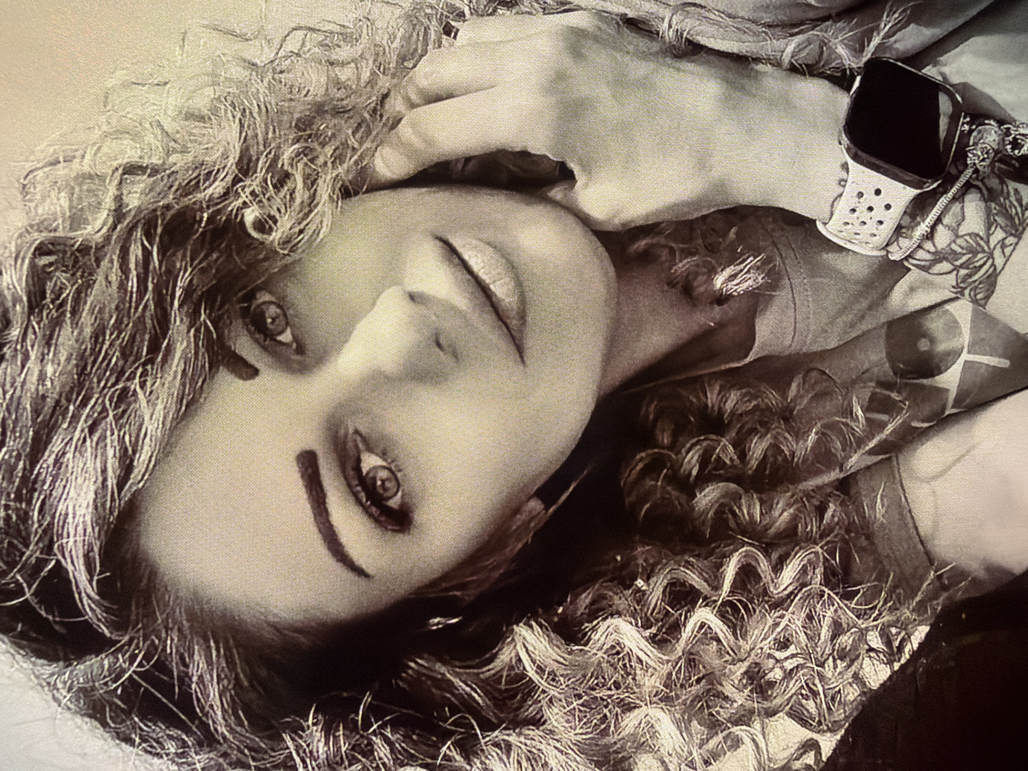 A sepia-toned photograph depicts a woman with curly hair lying down, her head tilted. She gazes upwards, with a hand near her temple. She wears a watch with a perforated band. The image does not provide information about the city of Dryanovo, Bulgaria.