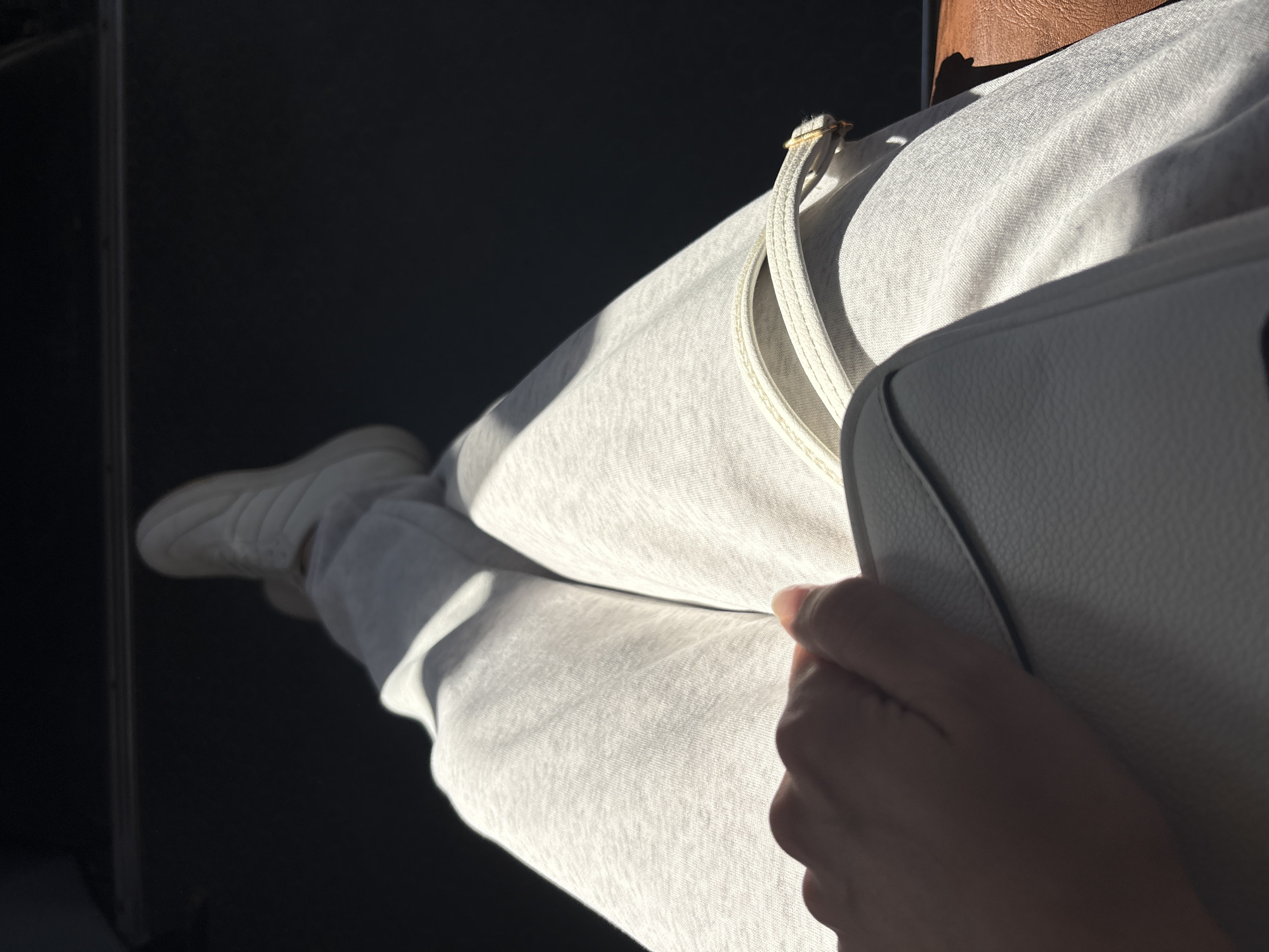 The image shows a person seated, wearing light-colored sweatpants and a white sneaker. A white bag is held in their hand. The scene appears to be indoors, with a dark surface visible to the left. The location, Chaikovsky, Russia, cannot be determined from the image alone.