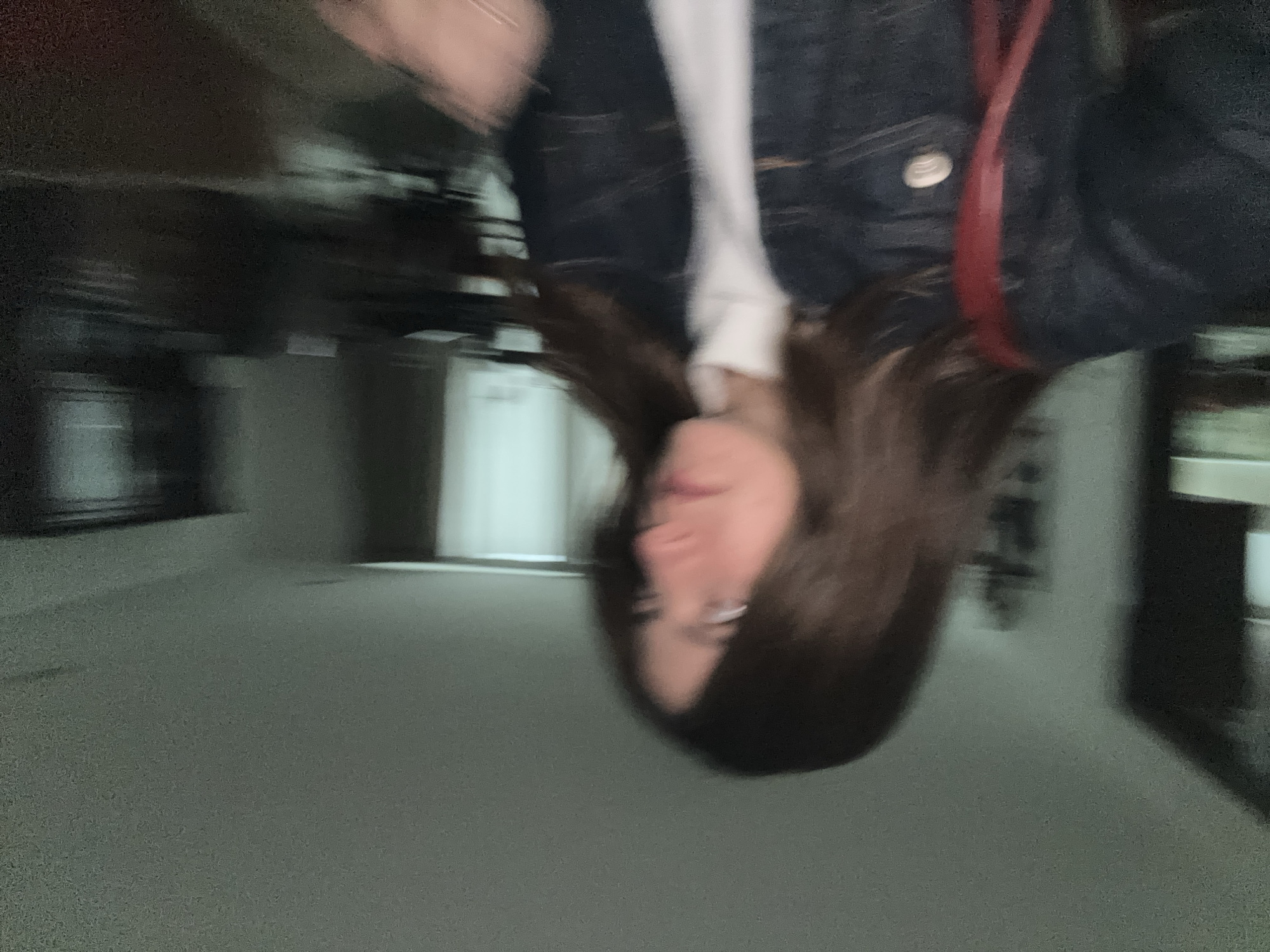 A blurred image of a person with long brown hair is oriented upside down in what appears to be a hallway or corridor. The person is wearing a denim jacket over a white top and a red strap crosses their torso. The background consists of a light gray floor and walls, with doors and possibly elevators visible. The location is likely indoors, possibly a building in an urban setting. Details specific to the city of Puebla, Mexico are not discernible from this image.