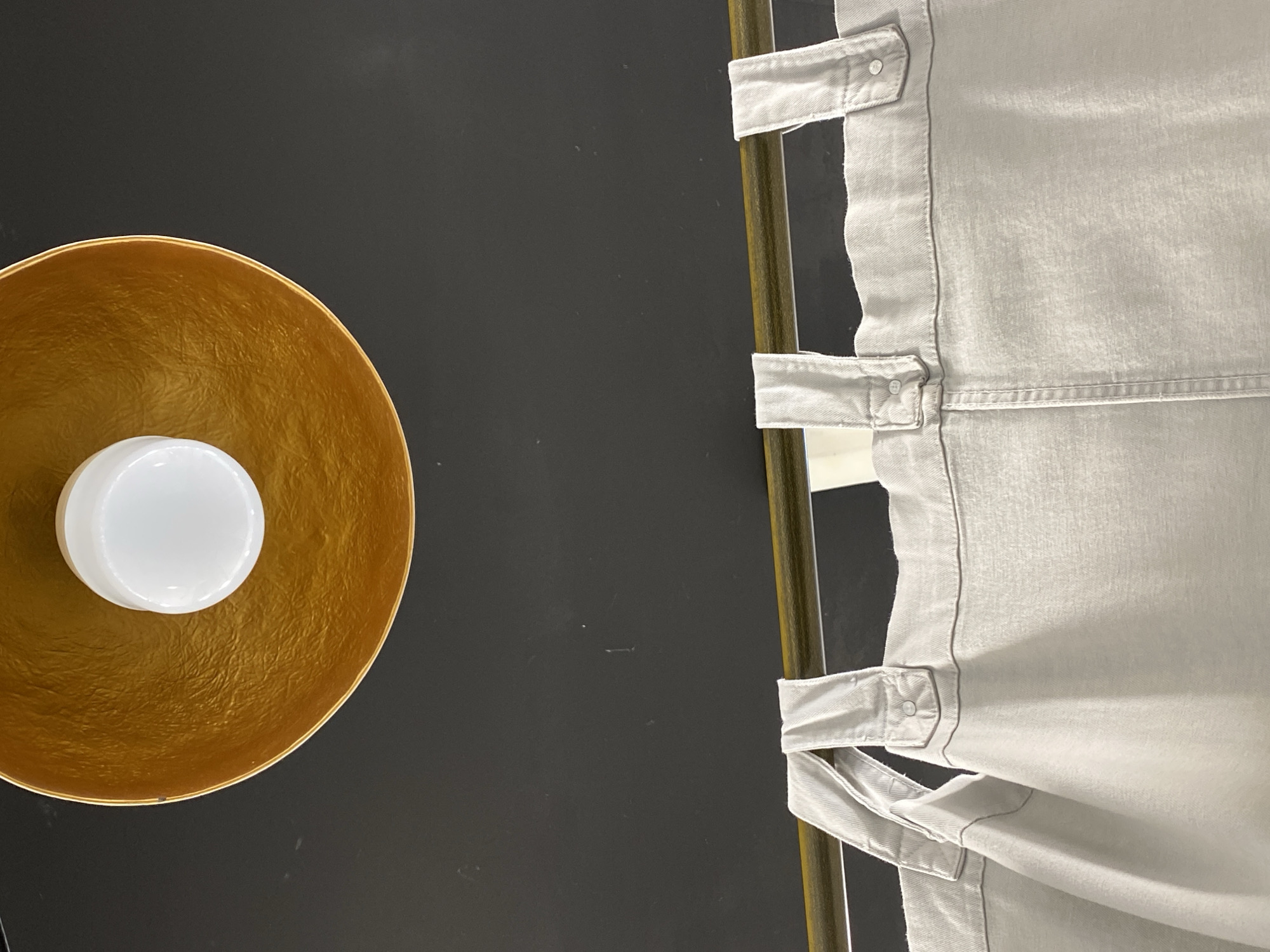 The image shows a top-down view of a scene featuring several objects. A gold-colored bowl with a white, spherical object inside is positioned on the left side of the frame. The background is dark and appears to be a flat surface. On the right side of the image, there is a light gray or white fabric or cloth with details such as straps or fasteners. A metal or wooden pole runs alongside the fabric.
The image does not show clear evidence to identify the city of Sochi, Russia.