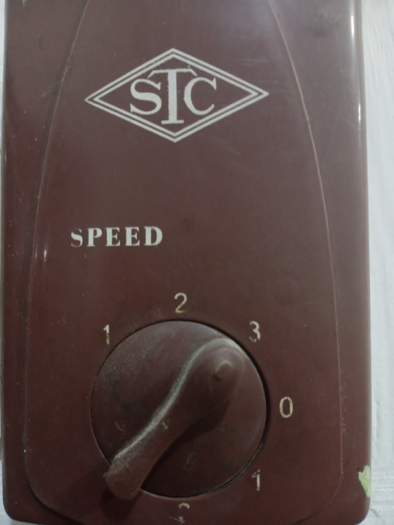 The image shows a close-up of a brown appliance with a diamond-shaped logo containing the letters "STC" in white. Below the logo, the word "SPEED" is written in white. In the center of the appliance is a circular dial with a knob, used for selecting speed settings. Numbers 0, 1, 2, and 3 are marked around the dial. The appliance appears dusty and is mounted on a white surface, possibly a wall. The scene is likely indoors. The location is identified as Jalingo, Nigeria.