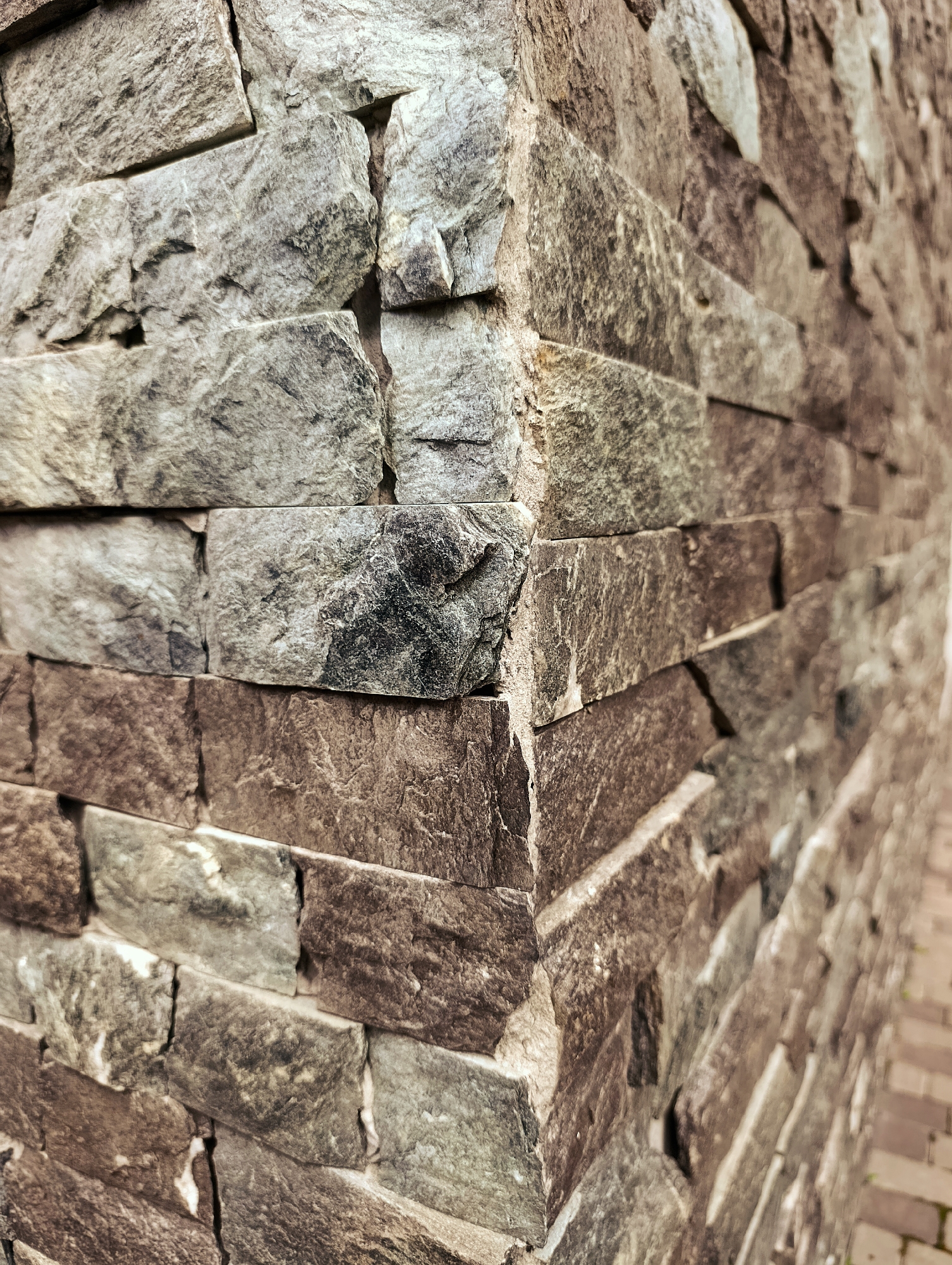 The image is a close-up, low-angle shot of a corner of a stone wall. The stones are rectangular and laid in a stacked, irregular pattern, giving the wall a textured, rustic appearance. The stones vary in color from light gray to dark brown and have rough, natural surfaces. The wall is constructed in Brovary, Ukraine, and appears to be an exterior feature, possibly part of a building or a garden wall. There are no people, animals, or visible signs of activity in the frame. The lighting suggests an outdoor setting during the day, with natural light casting subtle shadows that highlight the texture of the stone.