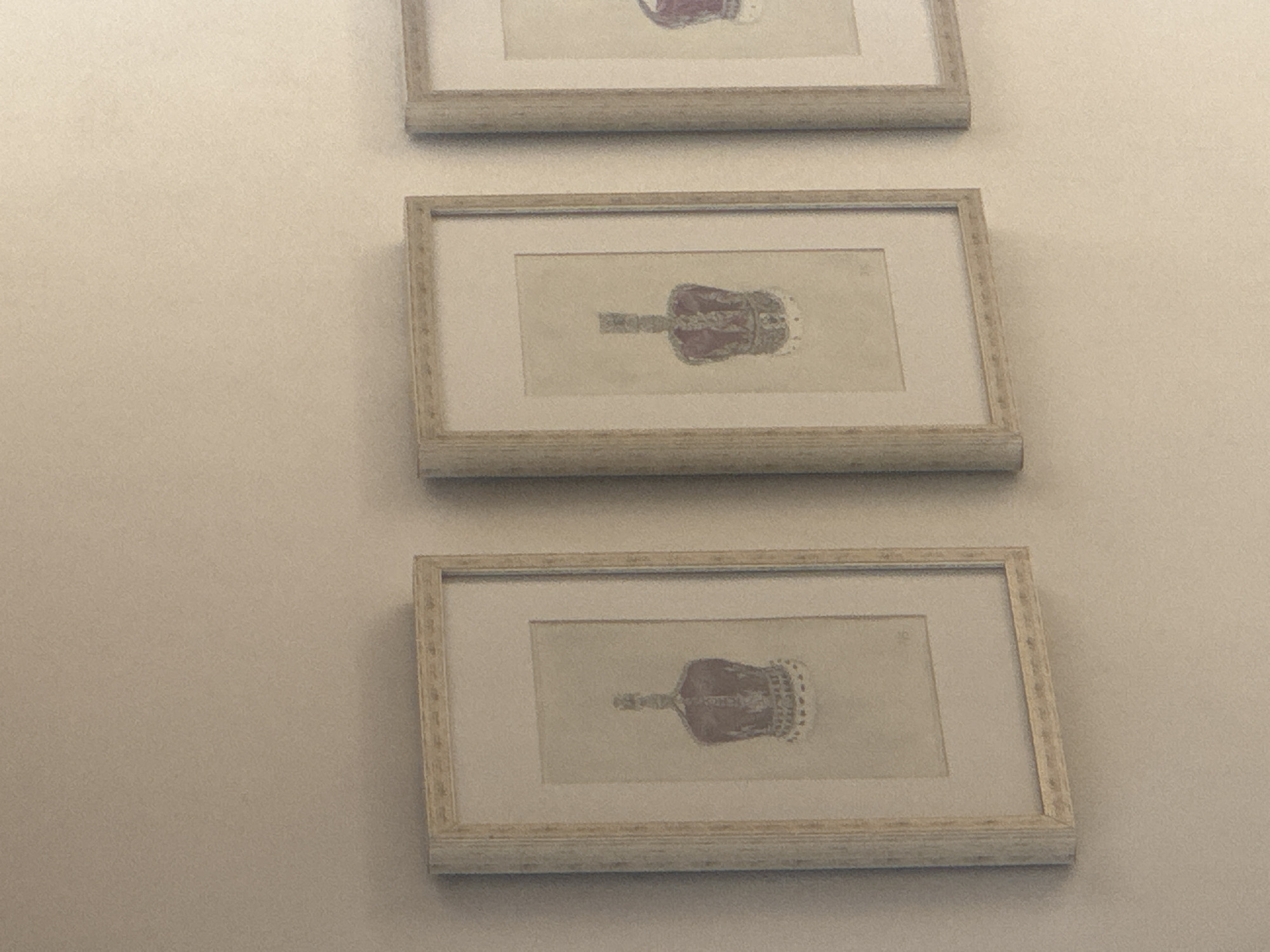 Three framed pictures of crowns hang on a light-colored wall. The location is unknown, but the request was to assume it is Puebla, Mexico.