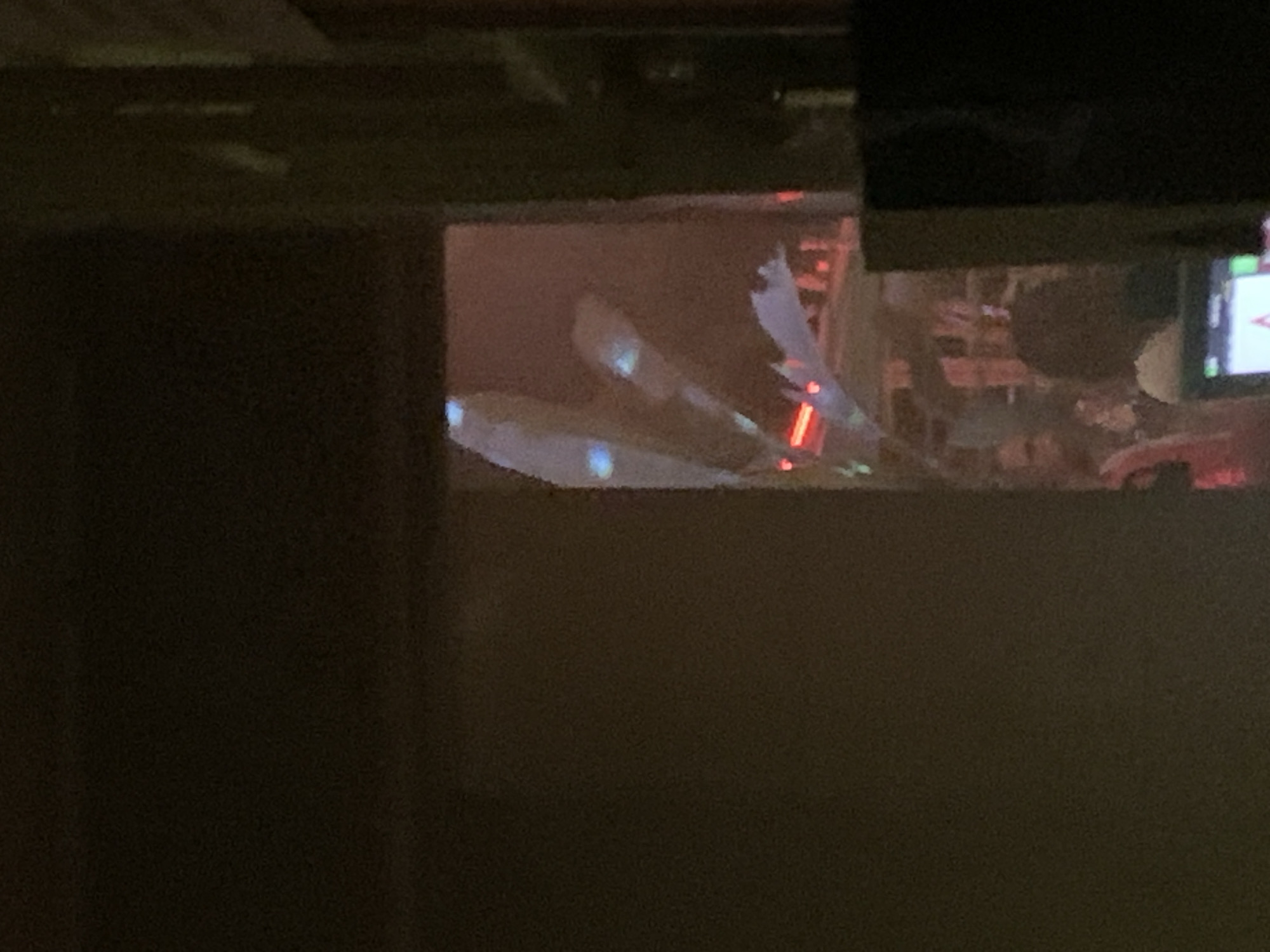 From an obscured viewpoint through a window or opening, the scene reveals elements suggesting a construction site or a partially completed building. There are indistinct figures and objects in the background, possibly workers and materials. The setting appears to be indoors, as suggested by the interior framing. The details lack clarity, preventing a conclusive identification of the subjects or specific location in Tel-Aviv, Israel.