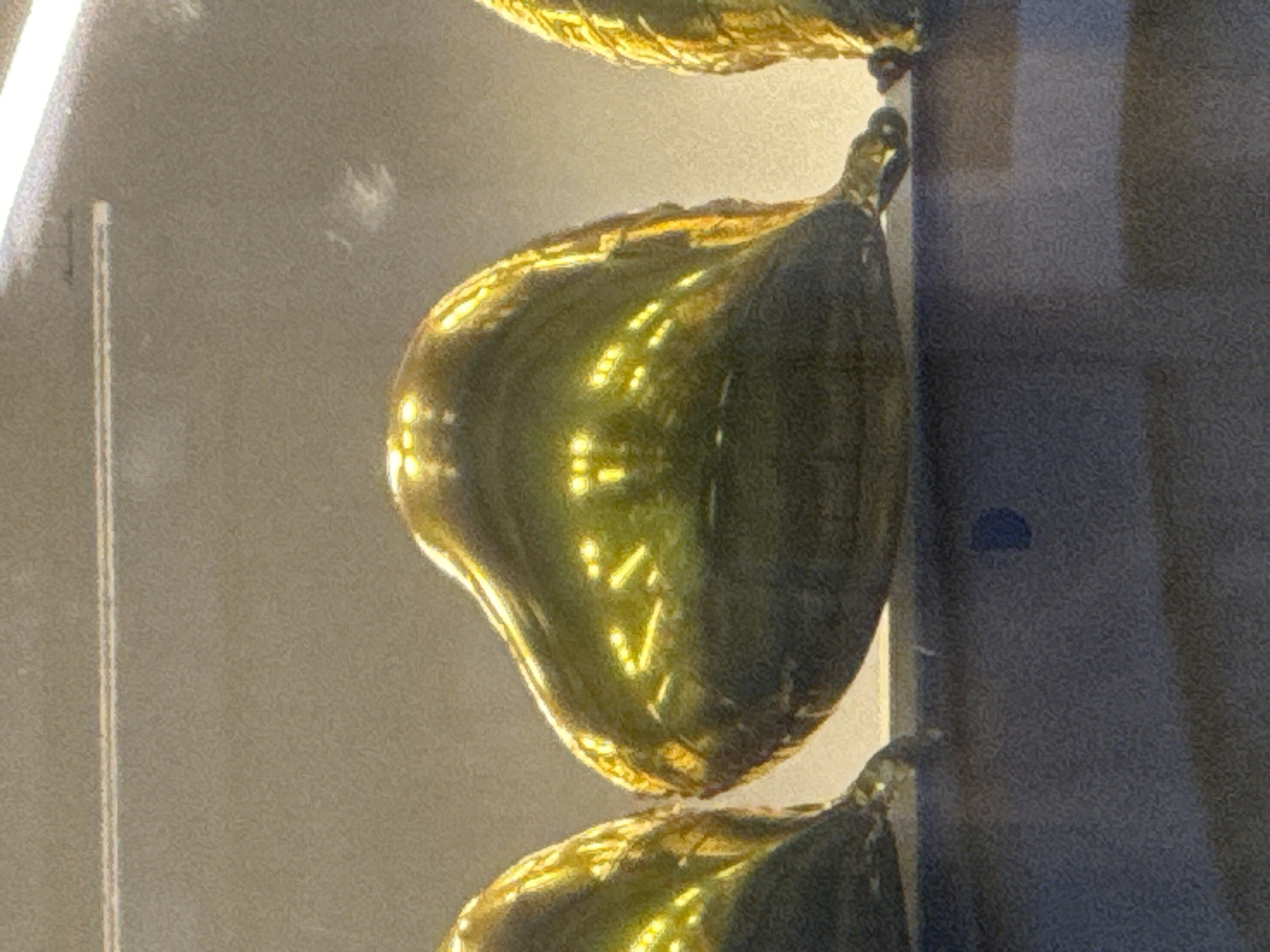 Three gold heart-shaped balloons are lined up on a dark surface. The balloons are reflecting light, creating bright, yellow patterns on their surfaces. The background is a neutral, light brown color. It is not possible to determine the location in Moscow, Russia, from the image.