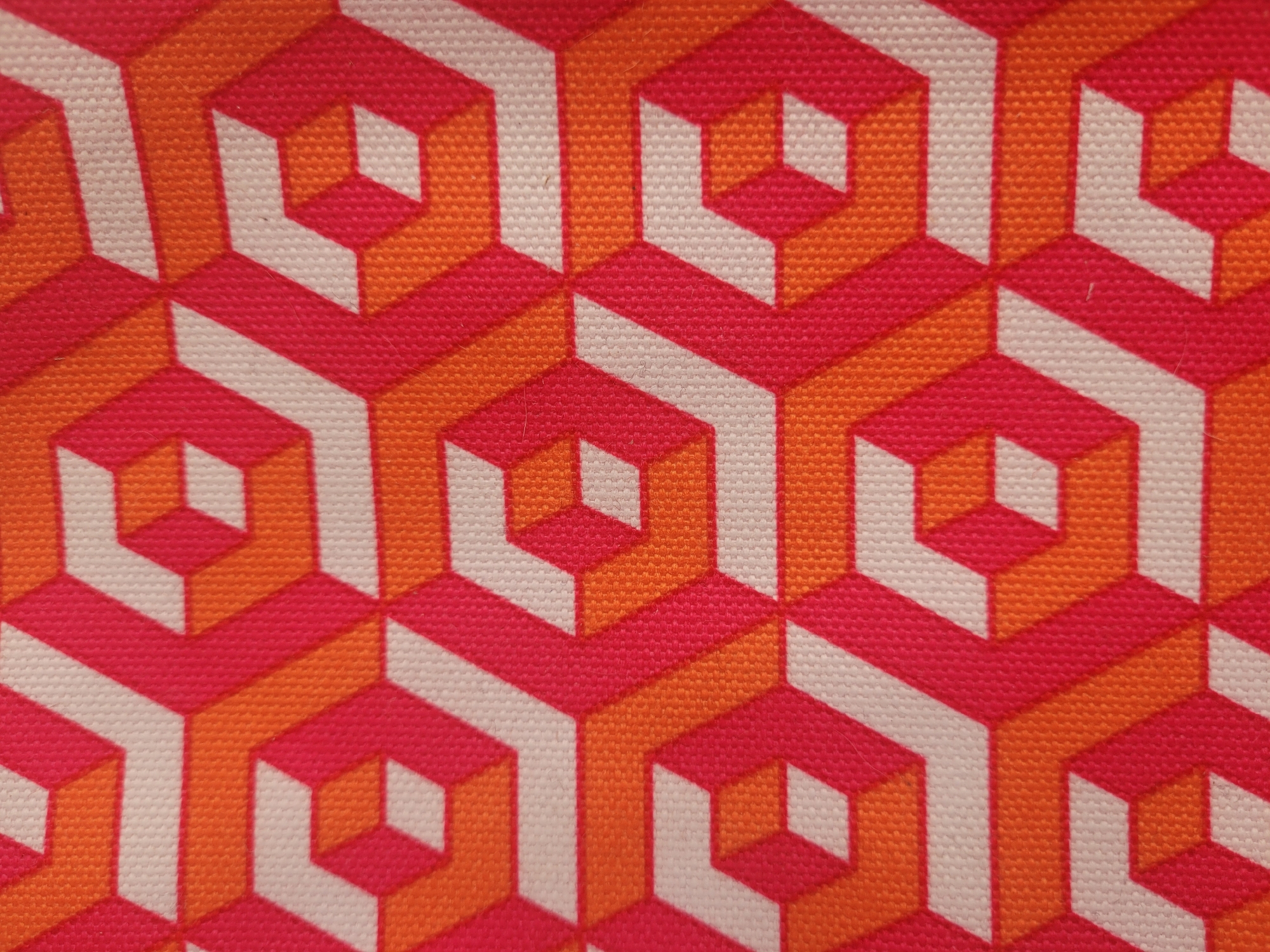 The image is a close-up, overhead shot of a fabric with a repeating geometric pattern. The pattern consists of interlocking hexagons rendered in shades of pink, orange, and white, creating an illusion of three-dimensionality. The fabric appears to be a canvas material with a visible woven texture. There is no indication of the city of Gävle, Sweden, or any other environmental or contextual information within the image.