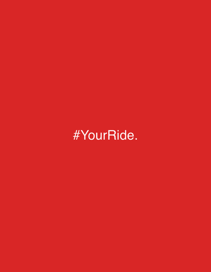 The image displays white text "#YourRide." against a solid, vibrant red background. The text is centered both horizontally and vertically within the frame of the main image. There are no other visible subjects, objects, people, or activities depicted. The scene is minimalist, focusing solely on the text and its bold background color. No specific time of day, weather, or explicit location cues are present within the image itself, though the context provided is Budva, Montenegro. The overall impression is clean, direct, and likely intended for branding, advertising, or a social media campaign.