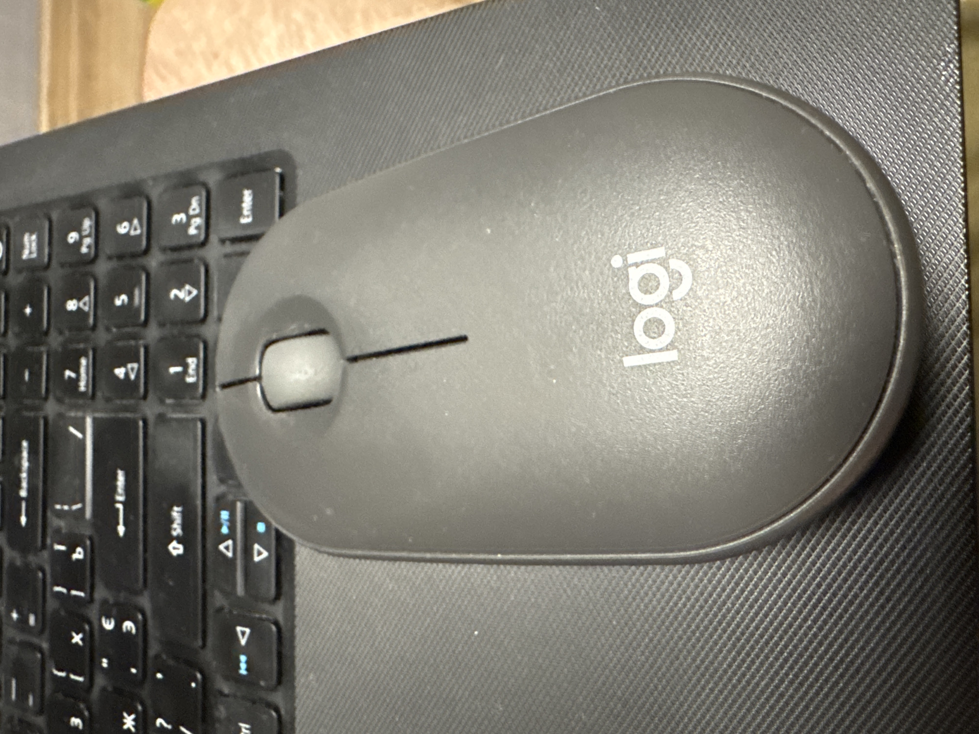 A gray Logitech computer mouse sits on a gray laptop computer near a keyboard. The keyboard appears to be black. A small portion of a brown surface is visible at the top of the image.
