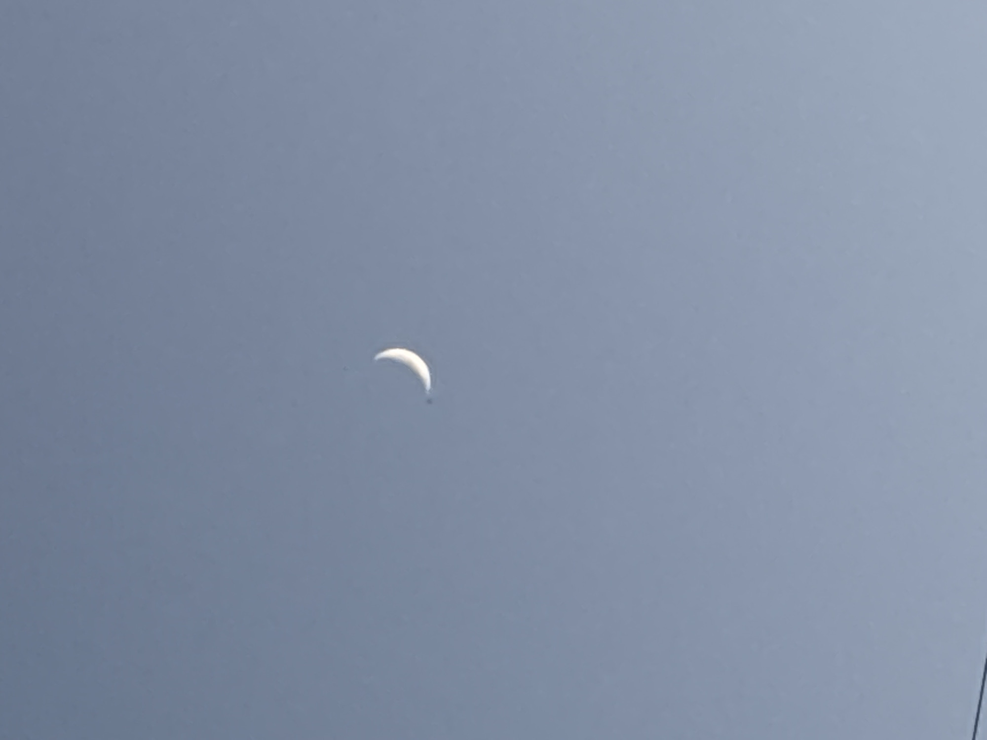 The image depicts a crescent moon in a clear, light blue sky. There is no indication of any specific location, including the city of Chaikovsky, Russia, or any people, subjects, objects, actions, or interactions beyond the moon in the sky.