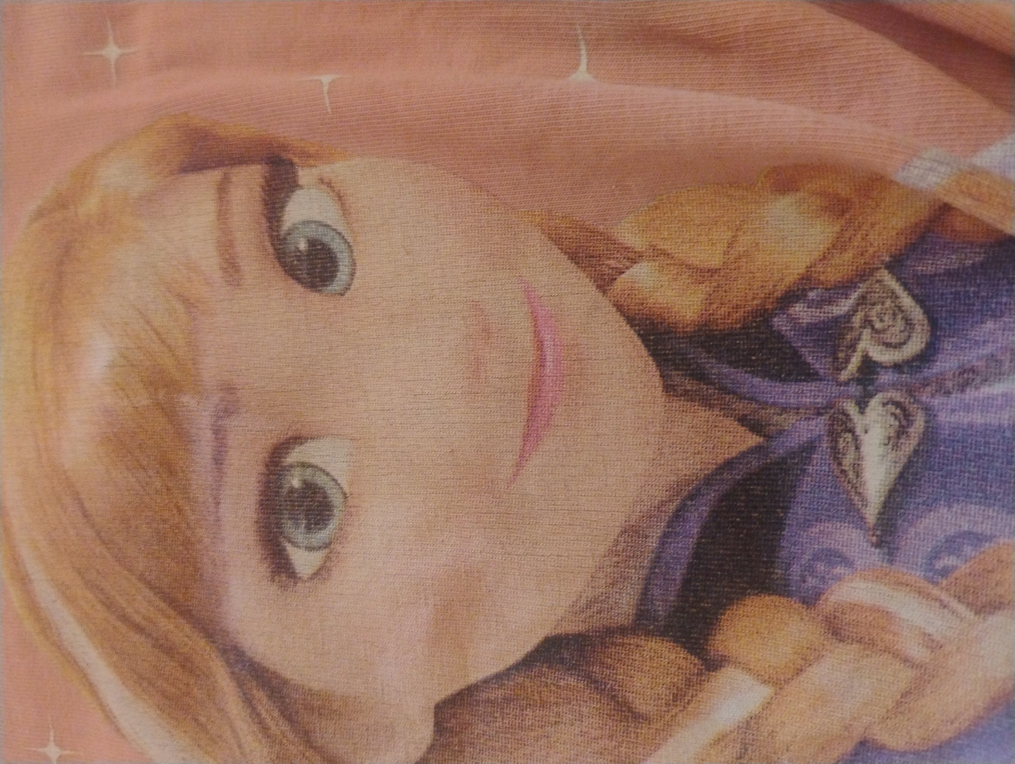 The image shows a close-up of a cartoon character's face. The character has blonde hair, blue eyes, and pink lips. The character is wearing a purple and blue outfit. The background is a solid pink color with some sparkly accents. There is no indication of the location being in Rumyantsevo, Bulgaria, or any other specific city. The image appears to be a print on fabric, possibly a t-shirt.