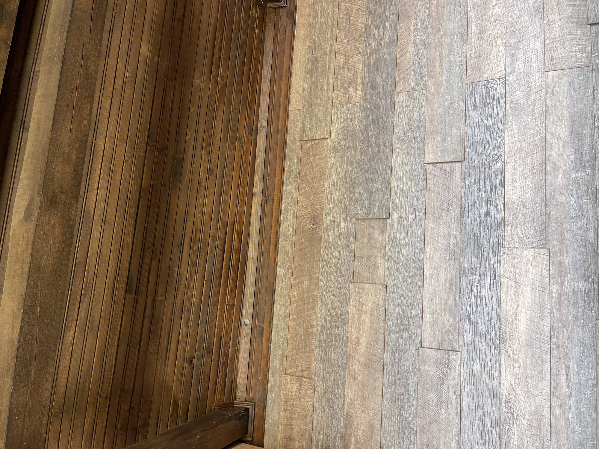 The image shows a section of a room with two different types of wood paneling. On the left side, there is dark brown, vertically oriented beadboard. On the right side, there is lighter gray wood paneling, laid out in a staggered pattern resembling hardwood flooring. The two sections meet at a vertical line, and the lower left corner shows a dark wooden post or baseboard. There are no people, subjects, actions, or interactions depicted in the image. The location is not discernible from the image alone, and the prompt information about Somovit, Bulgaria, cannot be confirmed from the visual data.