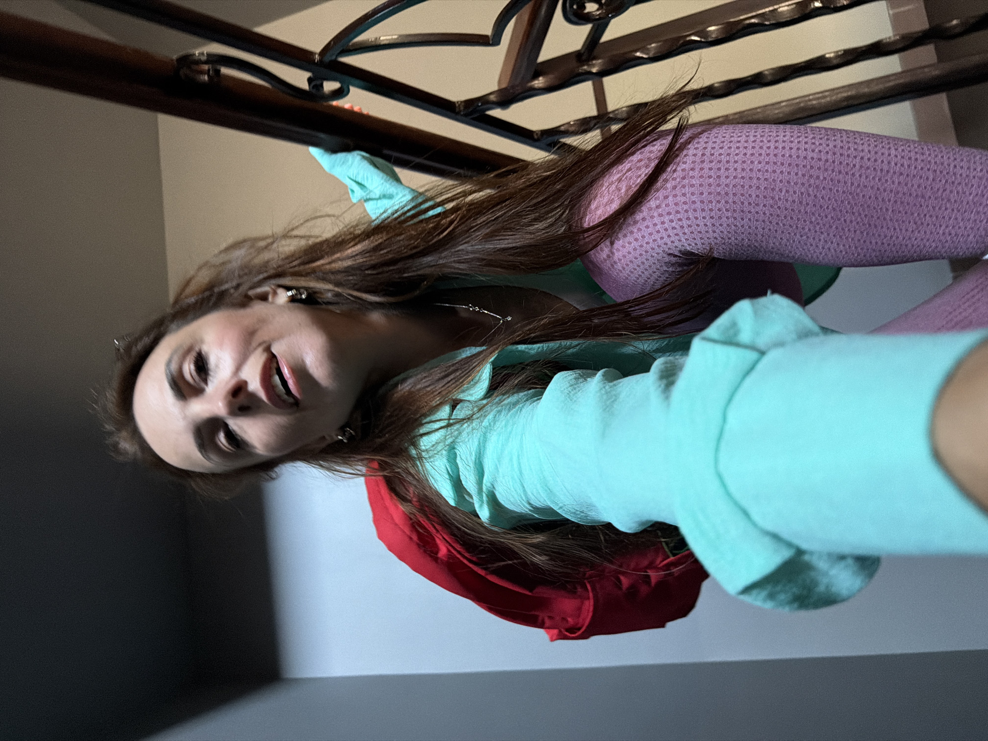 A woman with long brown hair, wearing a turquoise top and pink leggings, is photographed from a low angle on a staircase with a wooden handrail. She is holding a red backpack. The lighting suggests an indoor environment. The image does not contain any clues to indicate its location in Birobidzhan, Russia.