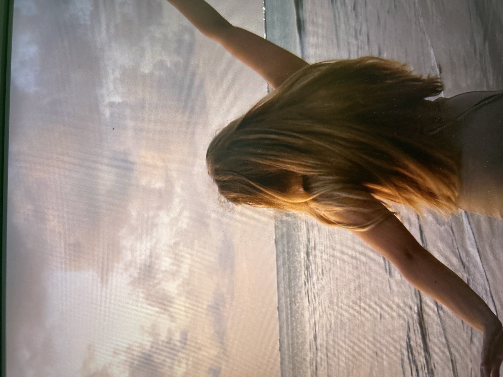 A woman stands on the beach with her arms outstretched. The sky is cloudy, and the water is calm. It is likely the location is in Kuta Selatan, Indonesia.