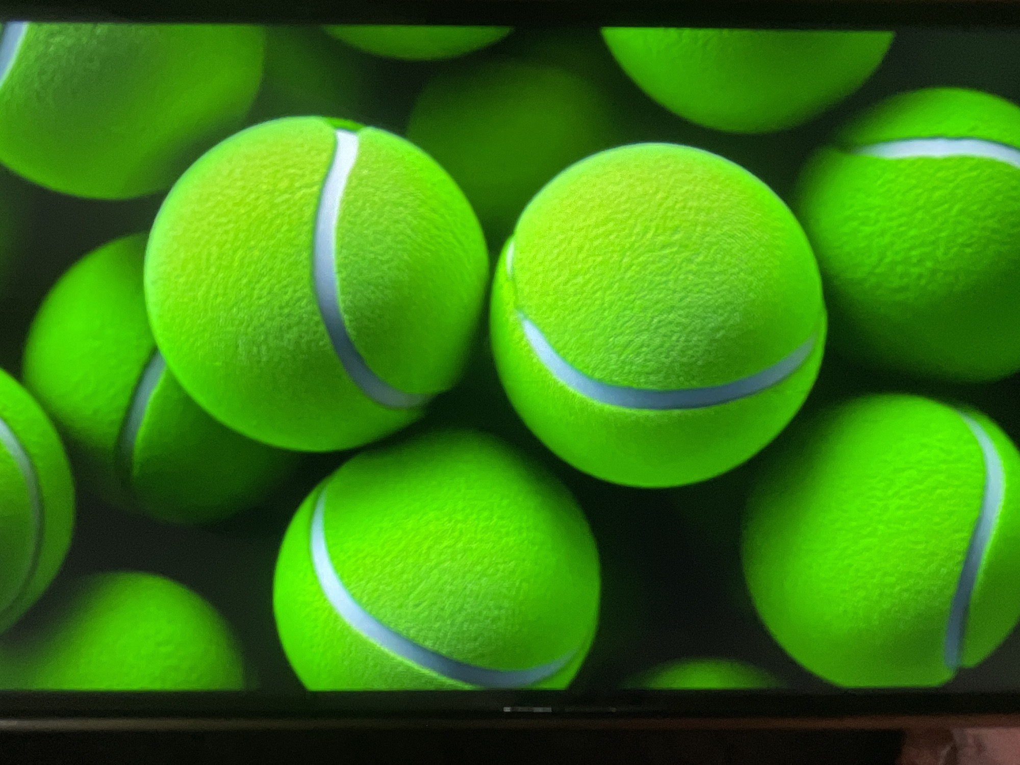 The image shows a close-up, vertical shot of multiple neon green tennis balls arranged in a pattern, some partially obscured by the edge of the frame. The tennis balls have a white curved line across their surface. The background is dark and out of focus, highlighting the vibrant color of the balls. There is no discernible location in Bishkek City, Kyrgyzstan.