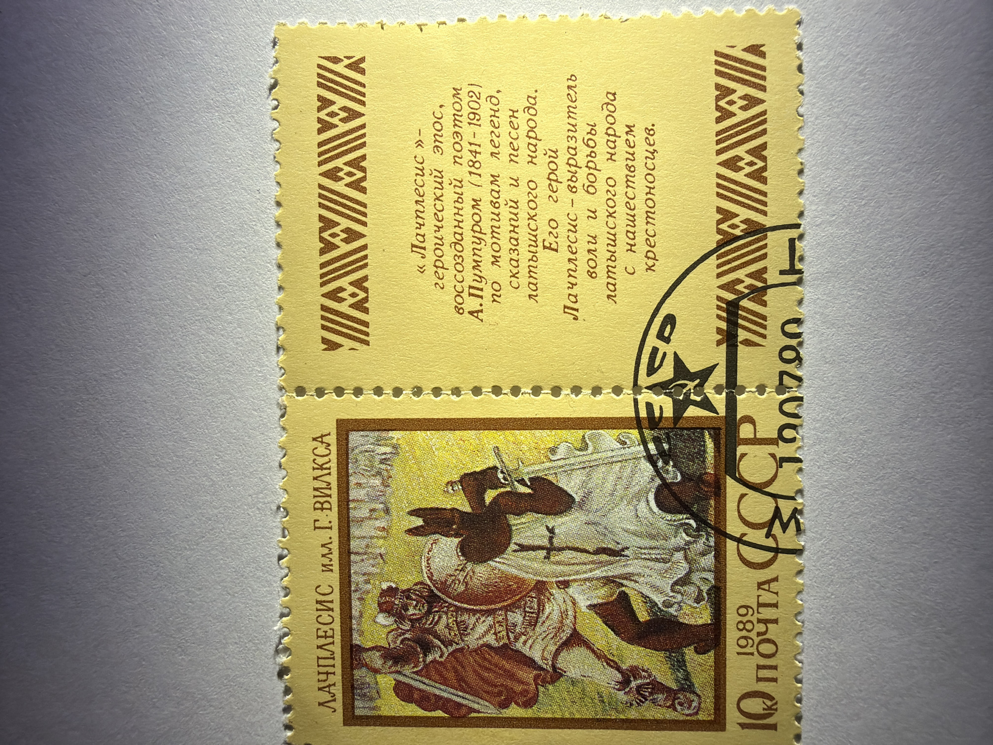 The image shows a USSR postage stamp from 1989. The stamp commemorates the Latvian epic hero, "Lāčplēsis" (Лачплесис), illustrated by G. Vilks. The lower stamp depicts a scene of Lāčplēsis in battle, wielding a sword and shield against an adversary. The upper stamp contains text in Russian describing Lāčplēsis as a hero who embodies the will and struggle of the Latvian people against the invading crusaders. It also mentions the epic poem "Lāčplēsis" recreated by poet A. Pumpurs (1841-1902), based on Latvian legends, tales and songs. The stamp has a face value of 10 kopecks. The stamp is postmarked with a partial impression of a stamp, including the last digits "00790" and the letters "ED"
There is no location of Izhevsk, Russia mentioned or shown in the picture.