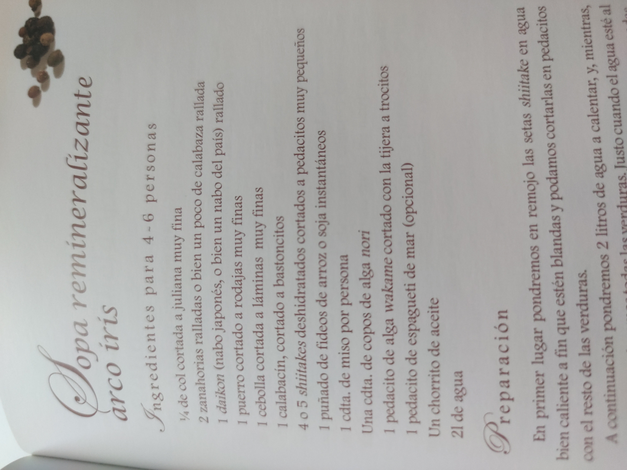 The image is a close-up of a page from a cookbook, featuring a recipe titled "Sopa remineralizante arco iris" (Remineralizing Rainbow Soup). The page lists ingredients for 4-6 people, including various vegetables, shiitake mushrooms, rice noodles, miso, nori, wakame, sea spaghetti, oil, and water. Below the ingredients, the "Preparación" (Preparation) section begins, describing the first steps of the recipe, which involve soaking the shiitake mushrooms in hot water. The text is in Spanish.
