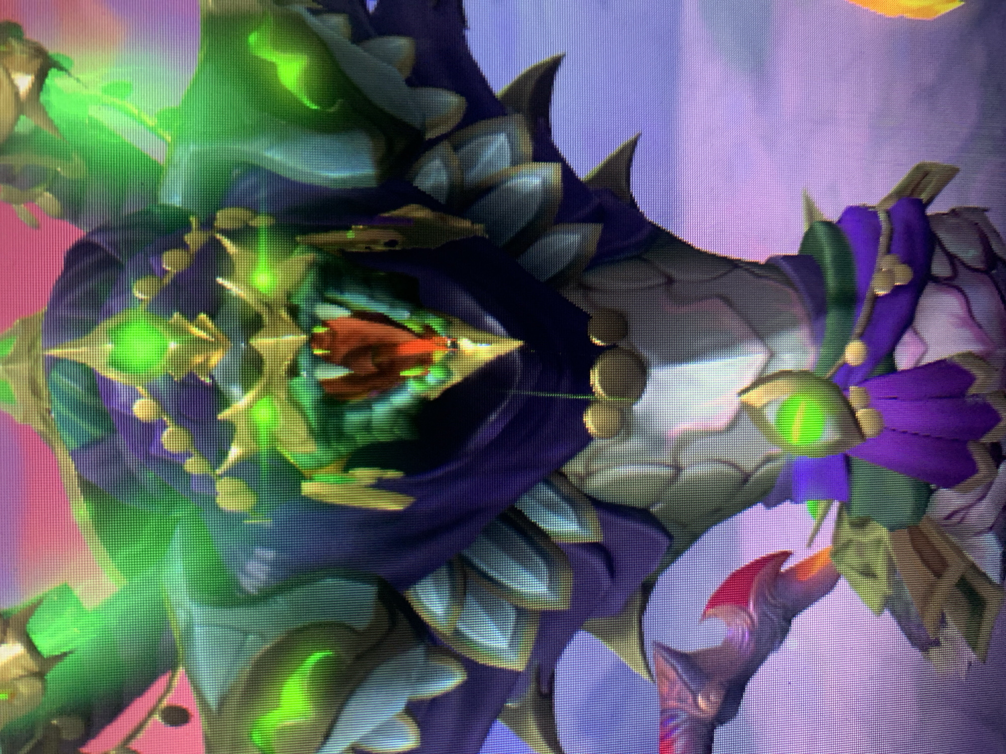 A close-up, medium shot captures the upper torso and head of a fantastical, serpentine creature rendered in vibrant digital art. The creature's head is in the center of the frame, with its mouth agape, revealing sharp, red teeth and a forked, pink tongue. Its eyes are large, luminous green orbs with sharp, angular pupils. The creature's head is adorned with a golden headdress featuring a prominent green gem at its center. Extending from its head and shoulders are multiple large, green, petal-like structures that glow with an internal light. The creature wears a dark purple cloak-like garment that drapes over its shoulders, accented with gold trim and circular gold embellishments. Below the head, its body is covered in segmented, pale grey armor with a textured, scale-like pattern, also edged with gold. A bright green, glowing eye is visible on its chest. Around its neck, a string of small gold spheres hangs. The background is a blurred gradient of pink, purple, and light blue, suggesting a sky at dawn or dusk. The overall impression is one of a mythical, possibly malevolent being. The image is pixilated, indicating it may be a screenshot of a video game or digital rendering.
