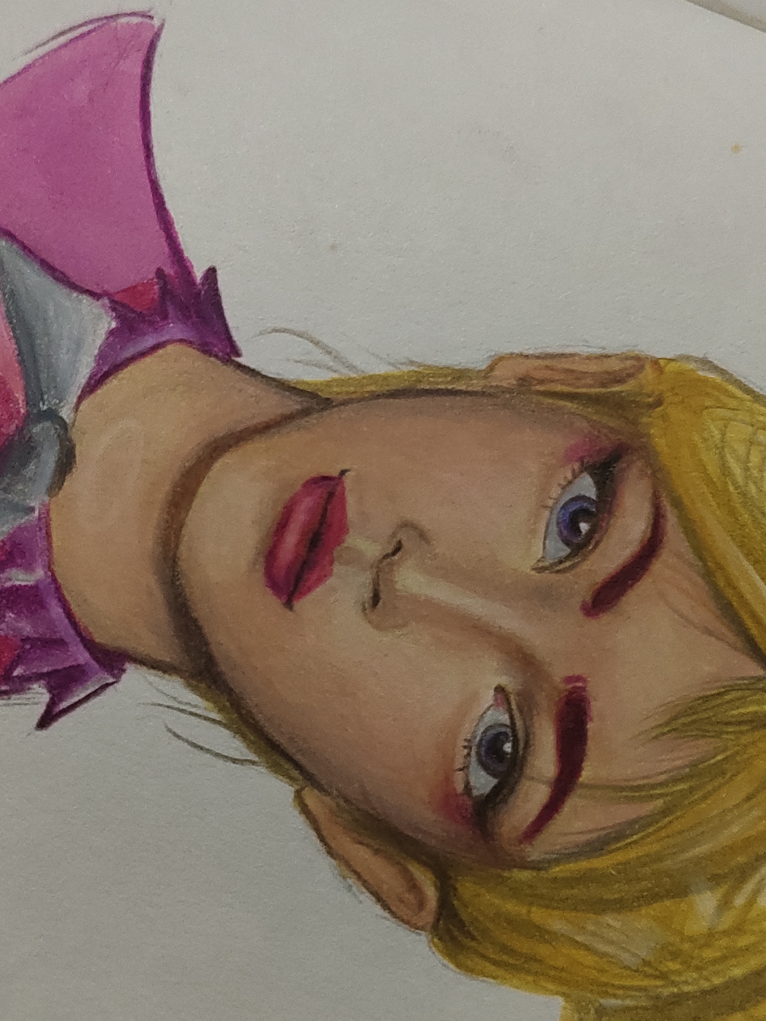 This image is a close-up photograph of a colored pencil drawing, rotated counter-clockwise. The drawing depicts a stylized character, likely female, shown from the upper chest to the head. The character has blonde hair rendered with yellow and light brown tones, fair skin with subtle shading, and open eyes with blue-purple irises, dark pupils, and visible white sclera. Reddish-pink makeup or pigment is applied around the lower eyelids and on the full lips. A distinct reddish, curvilinear mark is present on the character's right cheek. The attire includes a prominent pink, pointed garment or cape on the left side, layered over a grey element, and a ruffled purple collar around the neck area. The artwork is rendered on an off-white, textured paper surface, consistent with drawing paper, with minor discolorations visible in the plain background. The visual content of the image itself does not contain discernible elements identifying a specific location within Davao City, Philippines; the artwork is a portrait drawing.