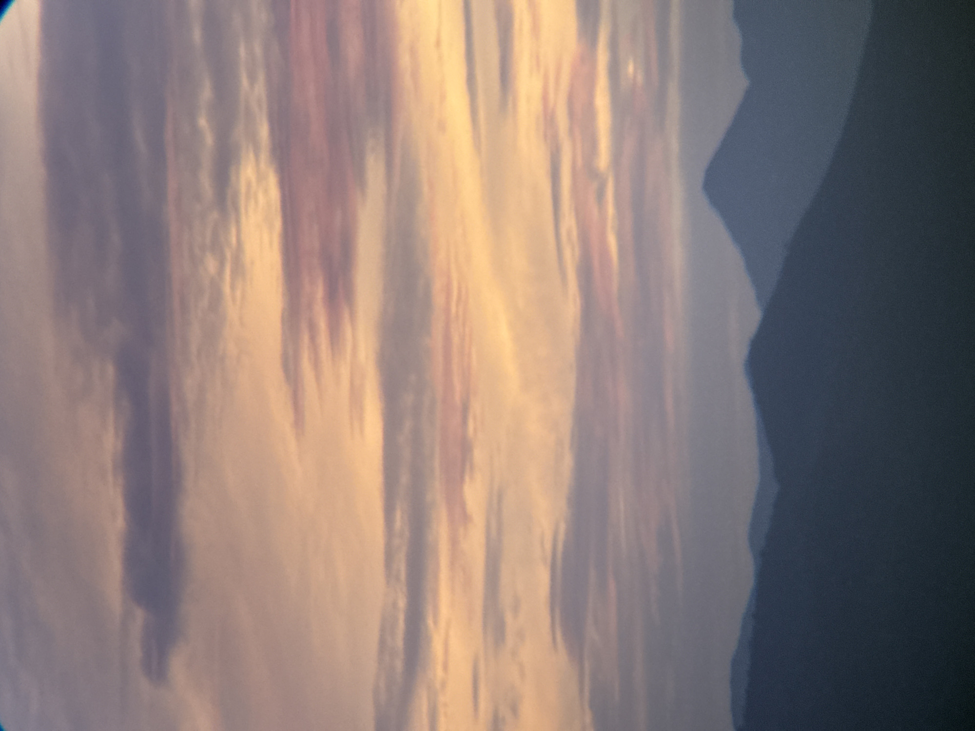 The image shows a serene mountainous landscape under a soft, pastel sky. Layers of subdued blue mountains recede into the distance, their peaks softened by atmospheric haze. The sky above is a canvas of muted oranges, pinks, and purples, indicative of either sunrise or sunset. Wispy clouds stretch horizontally across the frame, adding texture and depth to the celestial display. The overall impression is one of tranquility and natural beauty.
The specific location in Nha Trang, Vietnam, is not identifiable from the image itself. However, the scene depicts a common vista found in mountainous regions surrounding coastal cities, where the land meets the sea. Such landscapes are often associated with areas offering panoramic views, potentially from elevated viewpoints or specific mountain ranges within the province. Without further context or identifying landmarks, a precise location within Nha Trang cannot be determined.