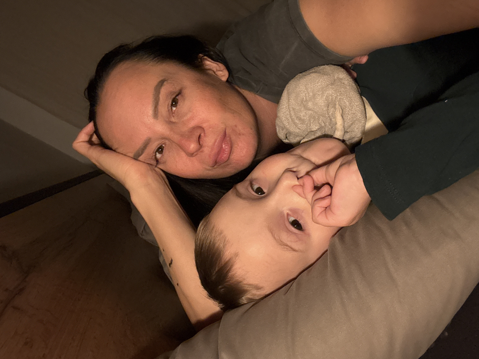A woman and a young child are lying down. The woman is lying on her side, with her head resting on her hand. The child is lying on a pillow. The woman is looking at the camera, and the child is looking up.
The photo was taken in Chaikovsky, Russia.