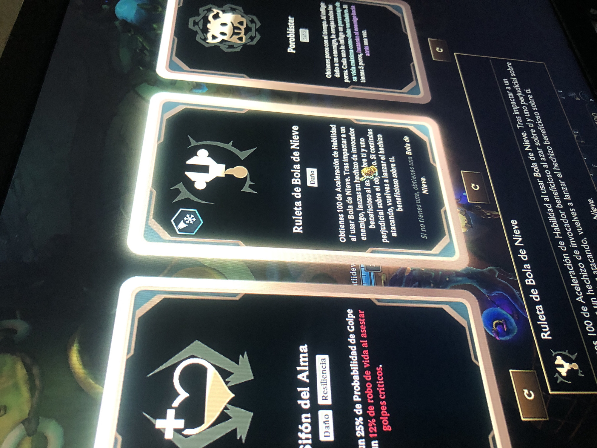 The image shows a close-up of a screen displaying in-game cards from a video game. The cards are laid out in a row, each with different titles and descriptions written in Spanish. The first card is titled "Sifón del Alma", categorizes it as "Daño" and "Resiliencia", and describes giving 25% Probabilidad de Golpe and 12% robo de vida al asestar golpes criticos. The second card is titled "Ruleta de Bola de Nieve" and categorizes it as "Daño". It describes a bonus in Aceleración de Habilidad after using Bola de Nieve, along with launching a helpful and harmful invocator spell. The third card is titled "Porobláster" and categorizes it as "Daño". It describes how the player obtains pores with time, and upon infligir daño a un enemigo will launch pores inflicting a percentage of their life. Parts of other text and card elements are also visible.