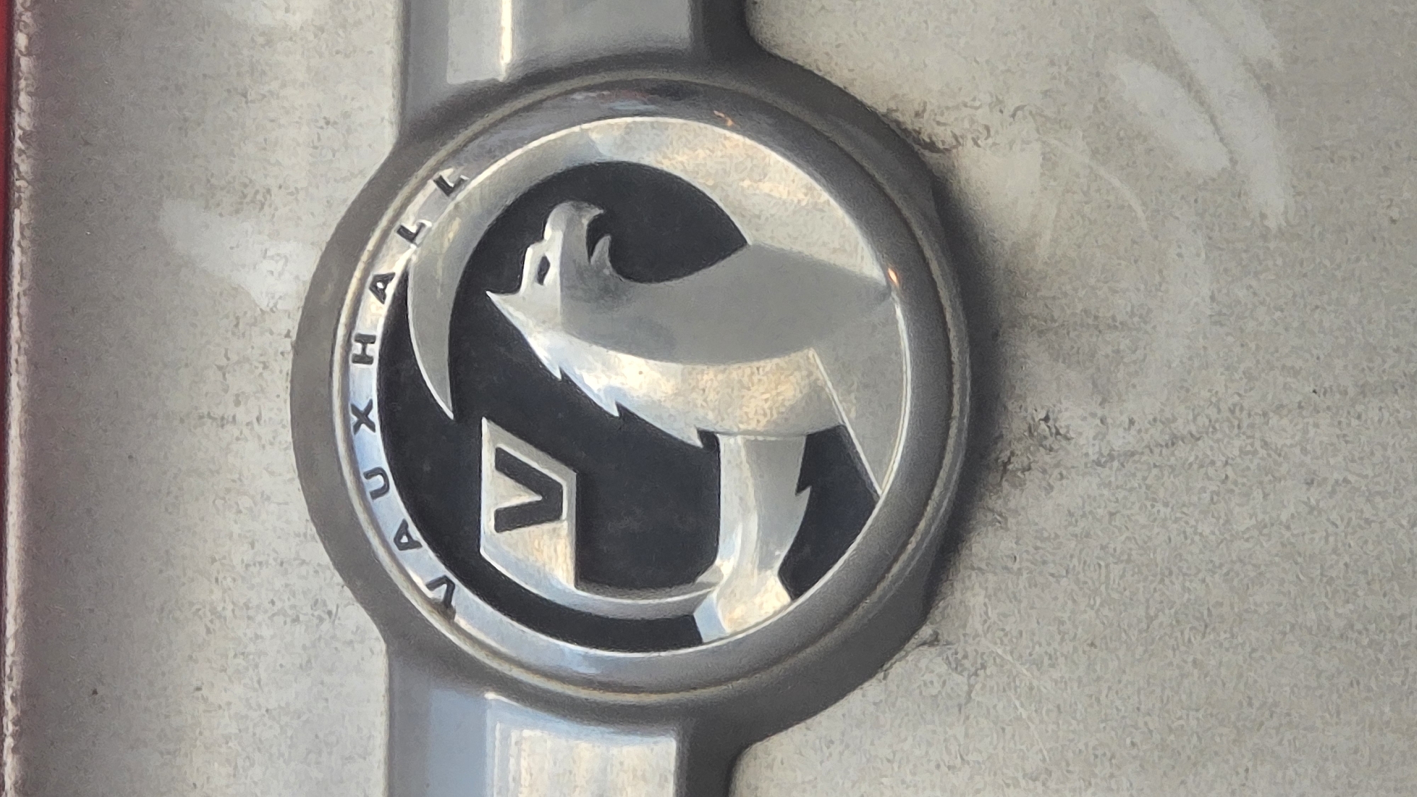 The image shows a close-up of a Vauxhall car emblem. The emblem is circular with a silver griffin inside a black circle. The word "VAUXHALL" is written around the edge of the black circle in silver letters. The emblem is mounted on a gray, slightly textured surface. The image does not provide enough information to determine the location in Sofia, Bulgaria, or any other details about the surrounding environment or any people present.