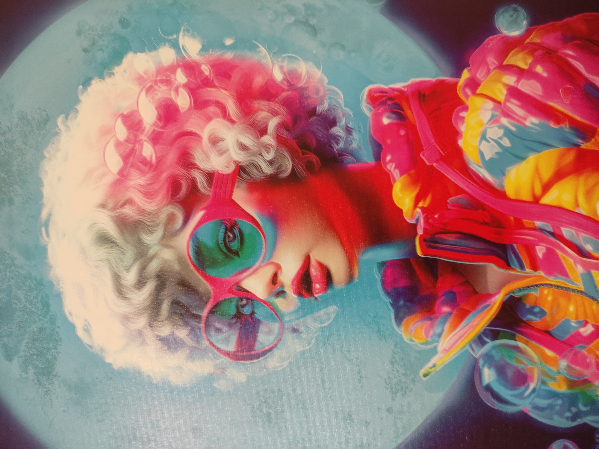 The image shows a surreal portrait of a person with curly white and pink hair and red-framed sunglasses with green lenses. The person has vibrant red lips and is wearing a colorful jacket with shades of red, orange, yellow, and blue. Bubbles surround the person, and a bluish-green background resembling a moon or a large bubble is behind them. The location is unknown.