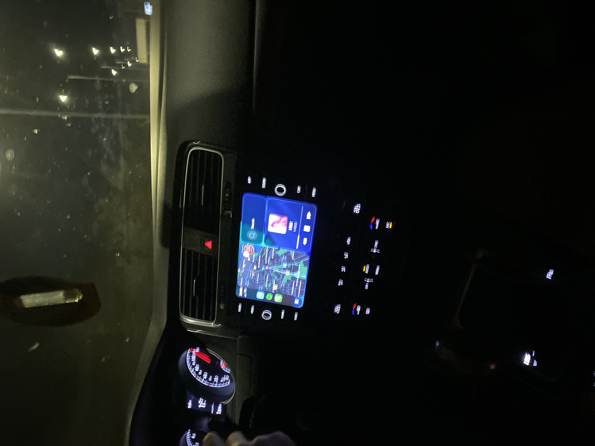 The image depicts the interior of a vehicle, likely a car, at night. The dashboard is visible, featuring an infotainment screen displaying a map, navigation, and music apps. Other dashboard elements include a hazard light button, air vent, climate control buttons, and a speedometer showing the vehicle is stationary. The time on the climate control screen is 22:35. The infotainment screen shows "RADIOID" and "HMNT VRGOD" in the title bar and "RADIO MEDIA PHONE VOICE" along the bottom. A person's hand is visible near the gear stick.
Without further information, I cannot determine the exact location in Varna, Bulgaria.