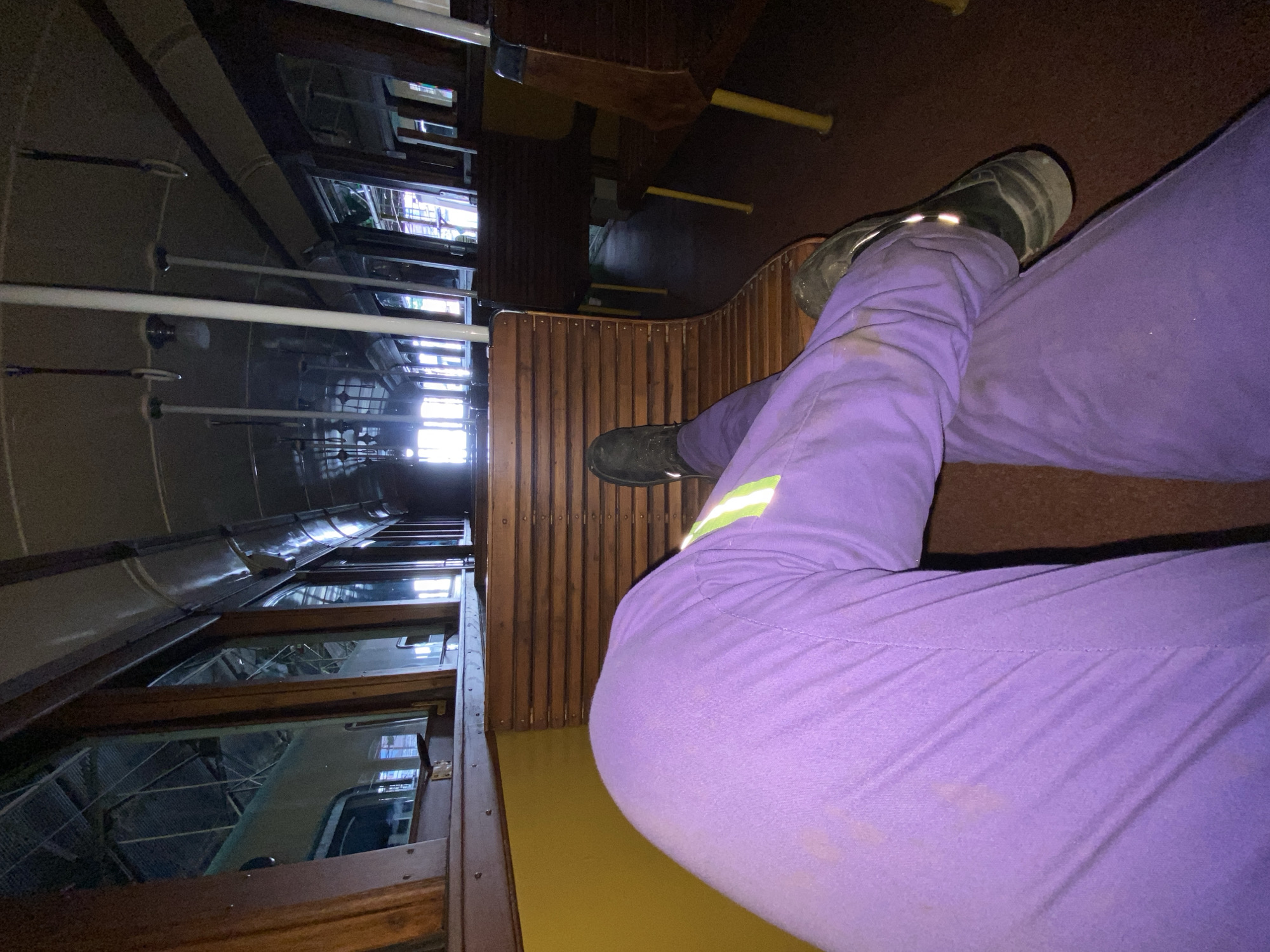 The image shows a person wearing purple pants and black shoes sitting on a wooden seat inside a vintage train car, likely a heritage tourist tram. The train car features wooden paneling, rows of windows, and overhead handrails. The scene is likely inside a tram of the Buenos Aires Historical Tramway in Argentina.