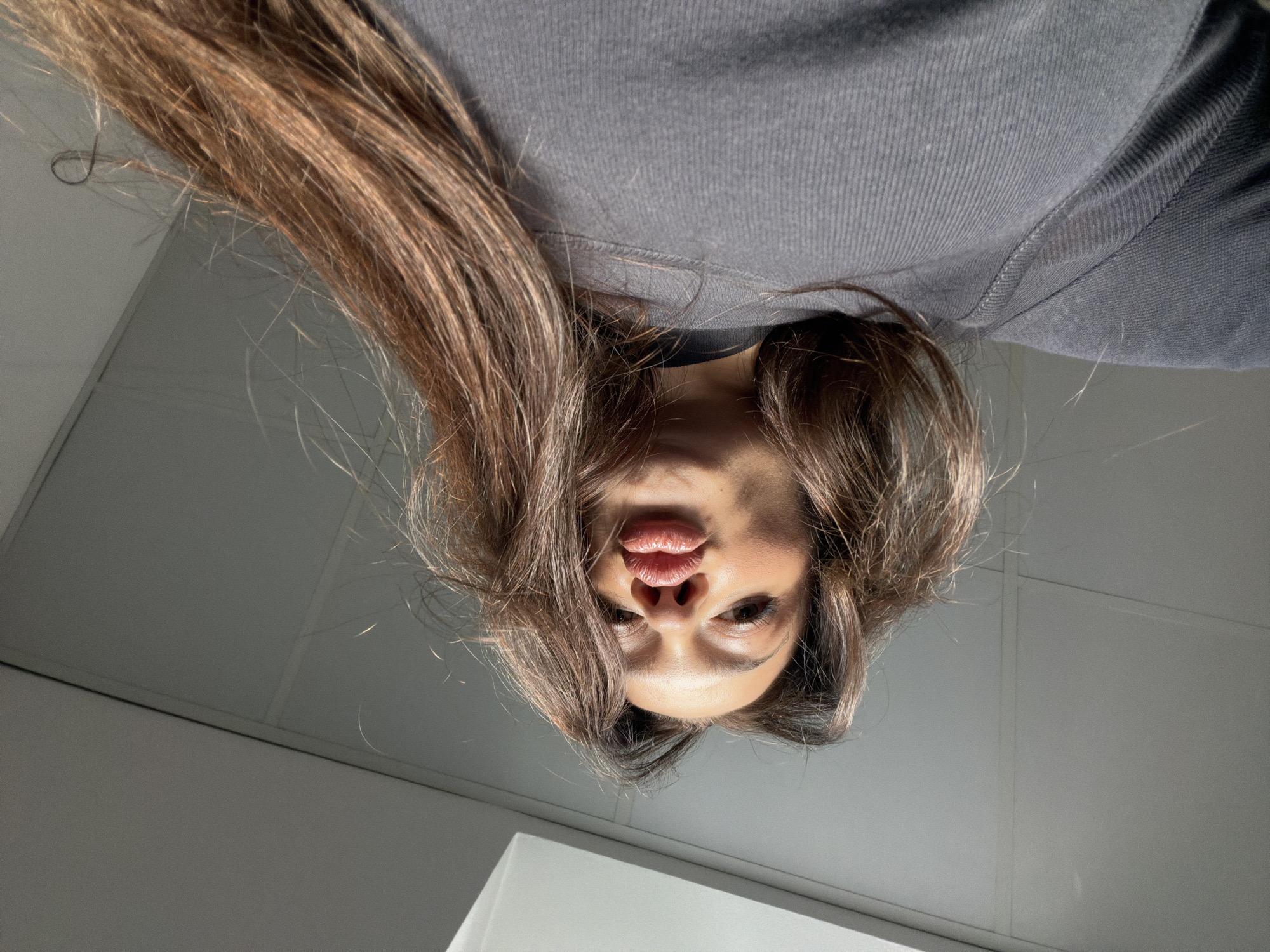 A woman with light brown hair and a grey sweatshirt looks down at the camera. The background is a white tiled surface. There is no visible information to indicate this photo was taken in Varna, Bulgaria.