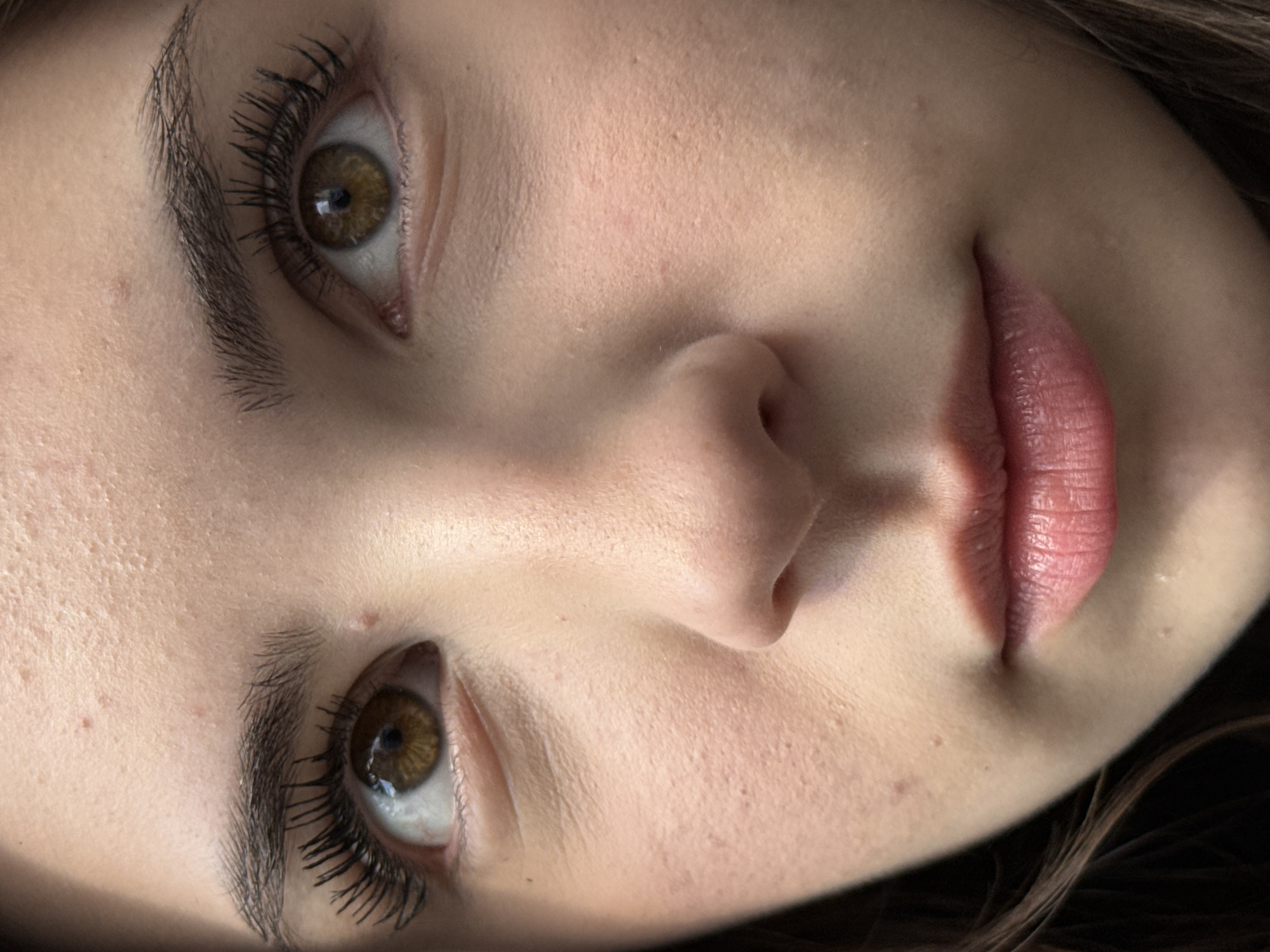 A close-up, rotated image shows a portion of a woman's face. The view includes her forehead, eyebrows, both eyes, nose, cheek, and lips. The woman has light skin, brown eyes, and brown hair. She is wearing mascara. The background is out of focus. There is no indication of location in Sofia, Bulgaria. The environment is not discernible.