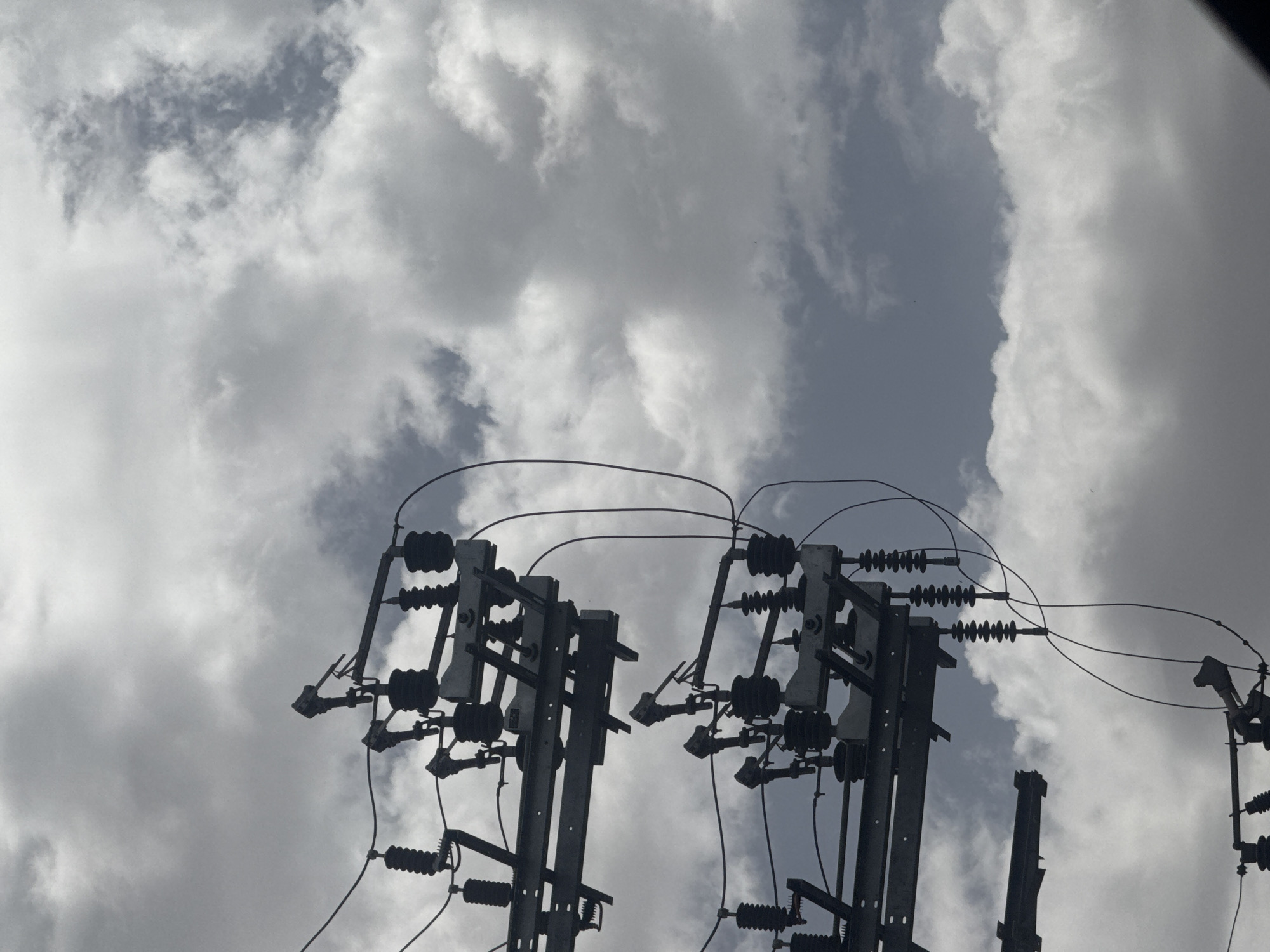 The image shows a view of utility poles with electrical wires against a cloudy sky. The utility poles are dark gray and appear to be metal, with various insulators and electrical components attached. The sky is filled with gray and white clouds, creating an overcast or stormy atmosphere. The image provides no information about the location being Tel-Aviv, Israel.