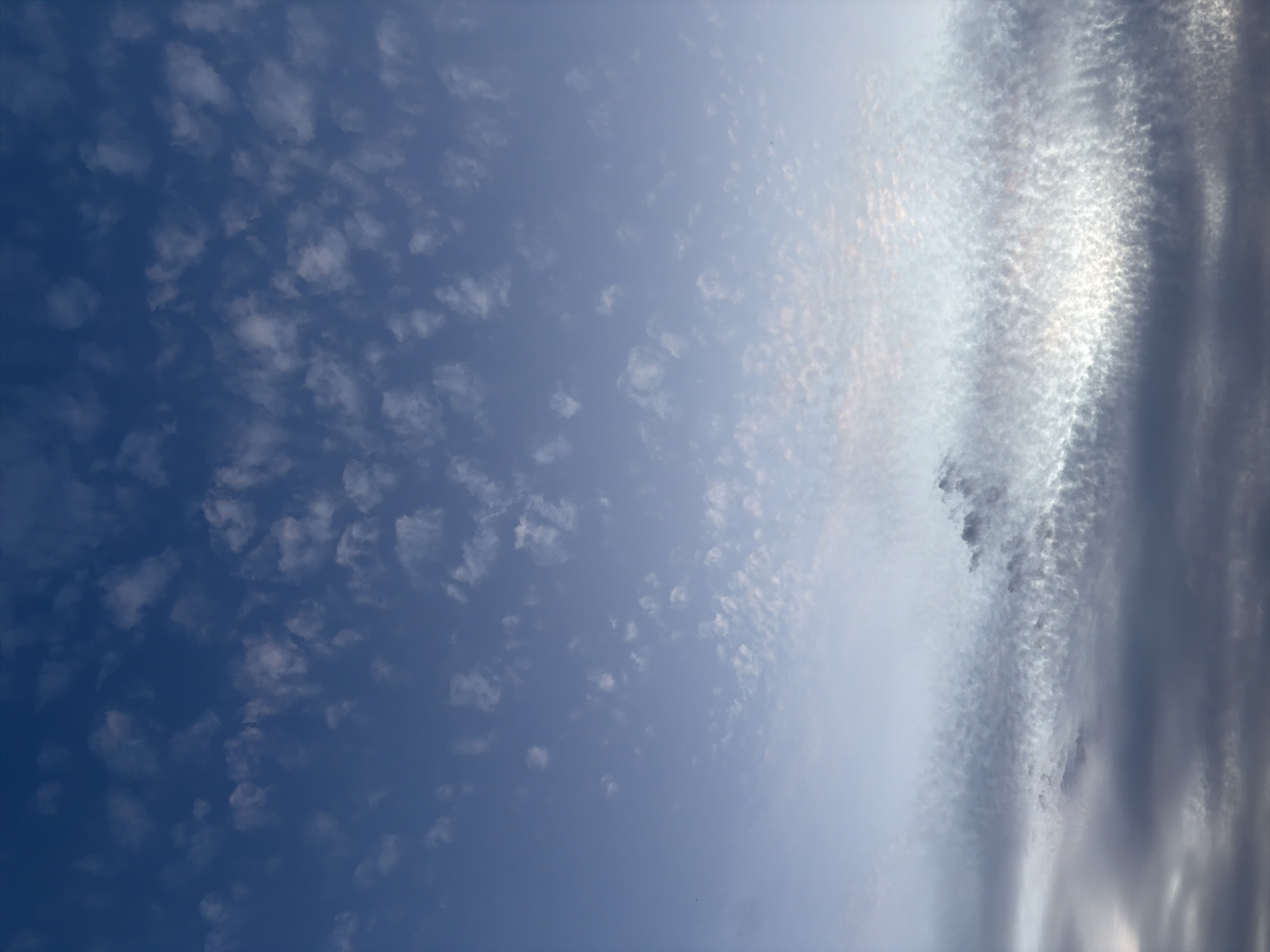 The image displays a clear sky with scattered clouds. The sky transitions from a deep blue at the top to a lighter, almost pale blue near the horizon. The clouds are a mix of white and light gray, with some appearing wispy and others more textured. The lower portion of the image features denser, darker gray clouds, creating a layered effect against the brighter sky above. There are no visible people, subjects, objects, or actions depicted in the image. The environment is solely the sky with varying cloud formations. The location is identified as Oxentea, Moldova.
