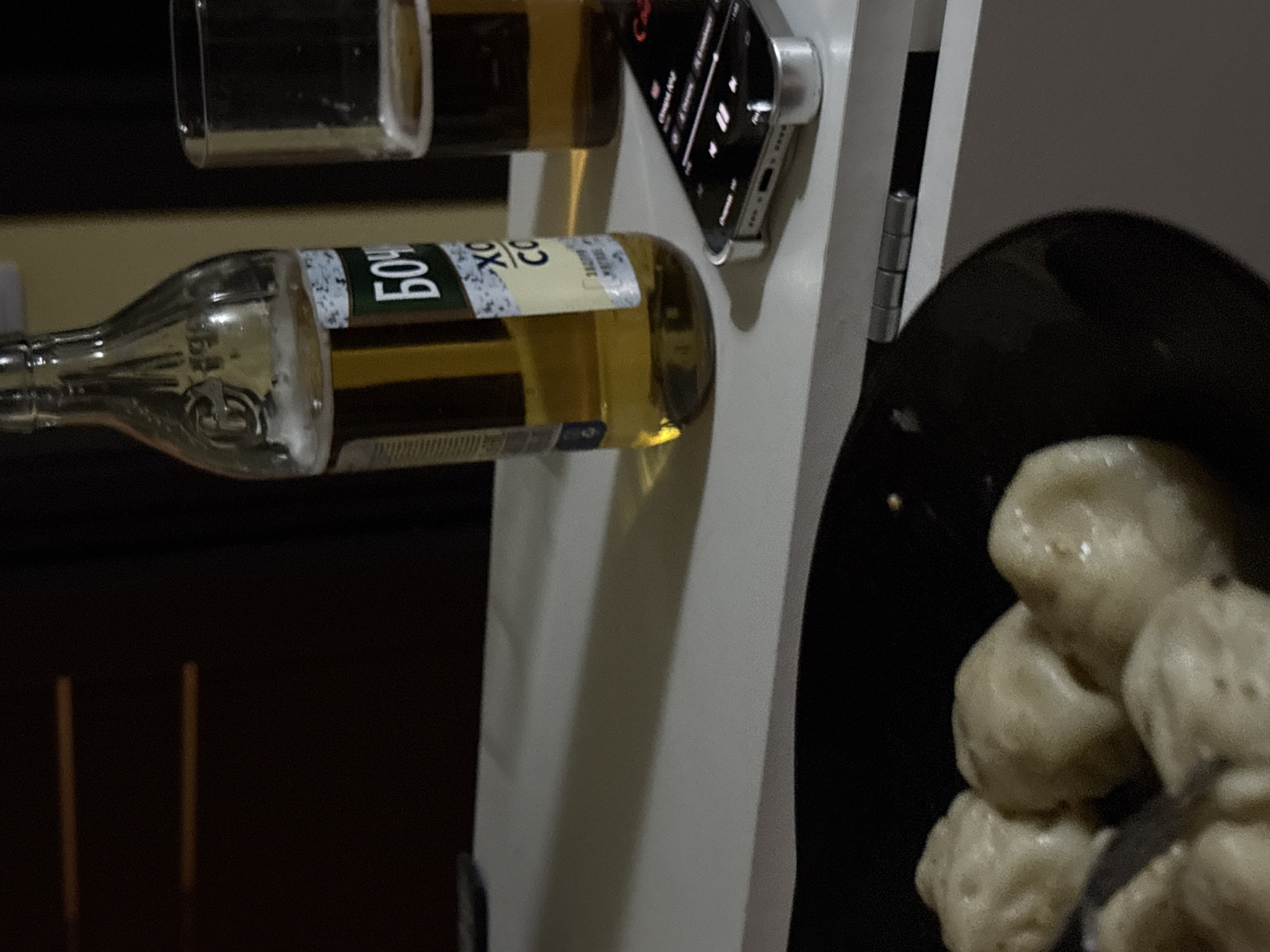 The image shows a bottle of Bochkarev beer and a glass of beer held on a white structure. An iPhone is mounted on the side of the structure. In the foreground is a black plate of food, possibly dumplings. The setting appears to be indoors. Ust-Ilimsk is not visually indicated.