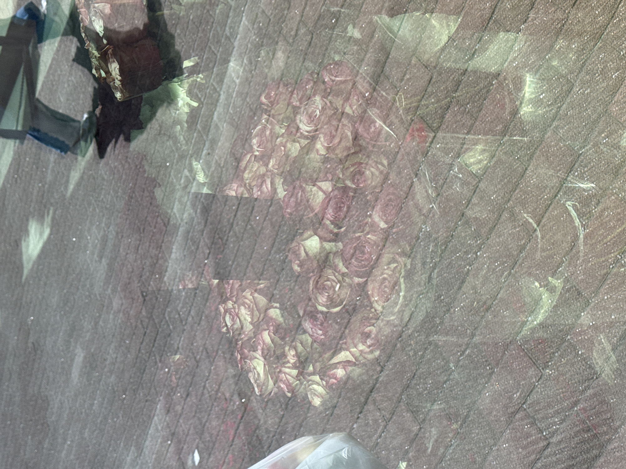 The image shows a bouquet of roses on the pavement, as seen through a dirty window. The location is unknown, and the image offers no evidence to suggest it is in Moscow, Russia.