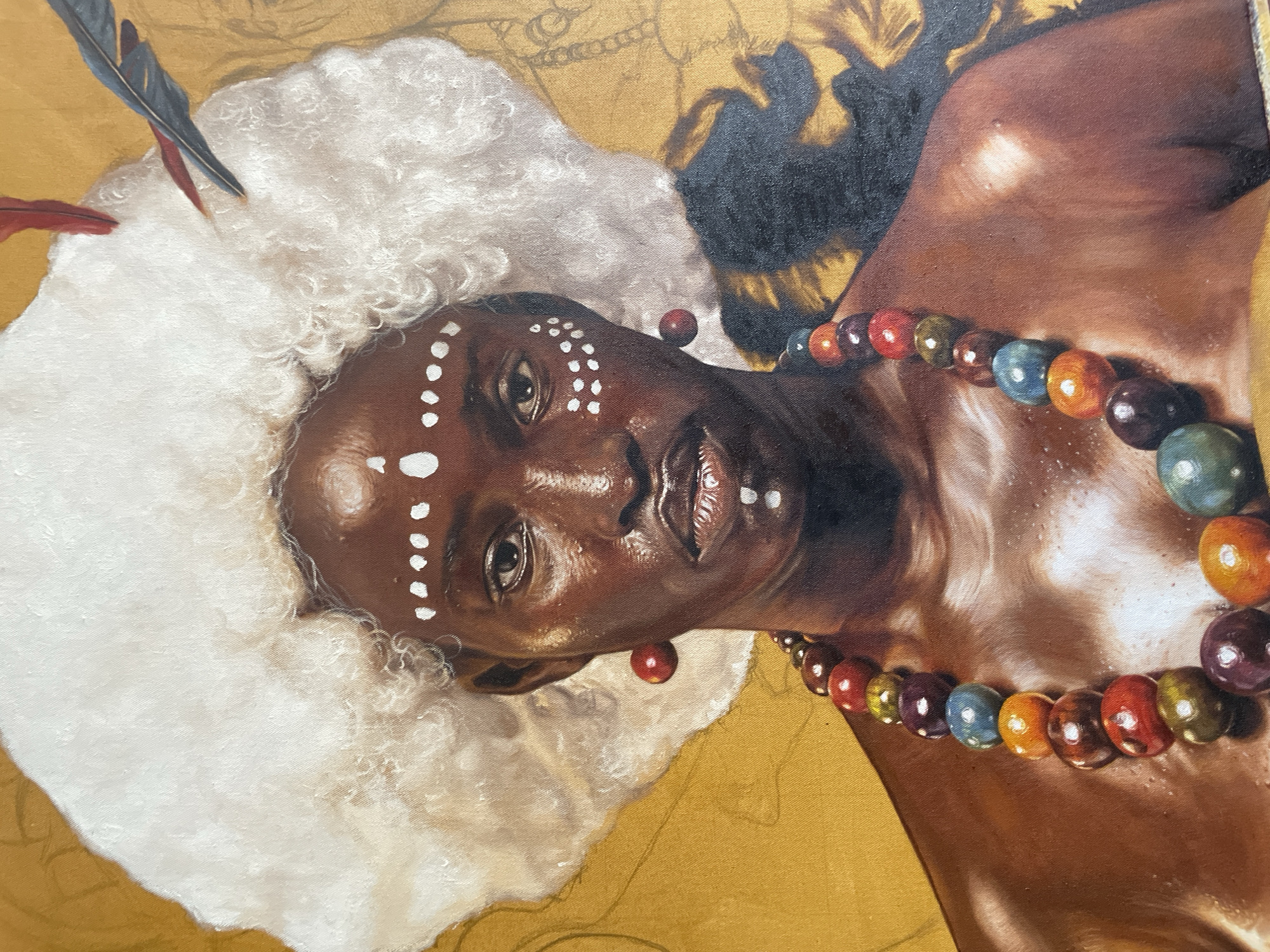 A portrait of a dark-skinned person with white markings on their forehead and around their eyes, wearing a white, fluffy headdress with feathers. A colorful beaded necklace adorns the neck. The background is a textured gold. The image is of a painting, but it is impossible to verify its location in Ado, Nigeria, based solely on the image.