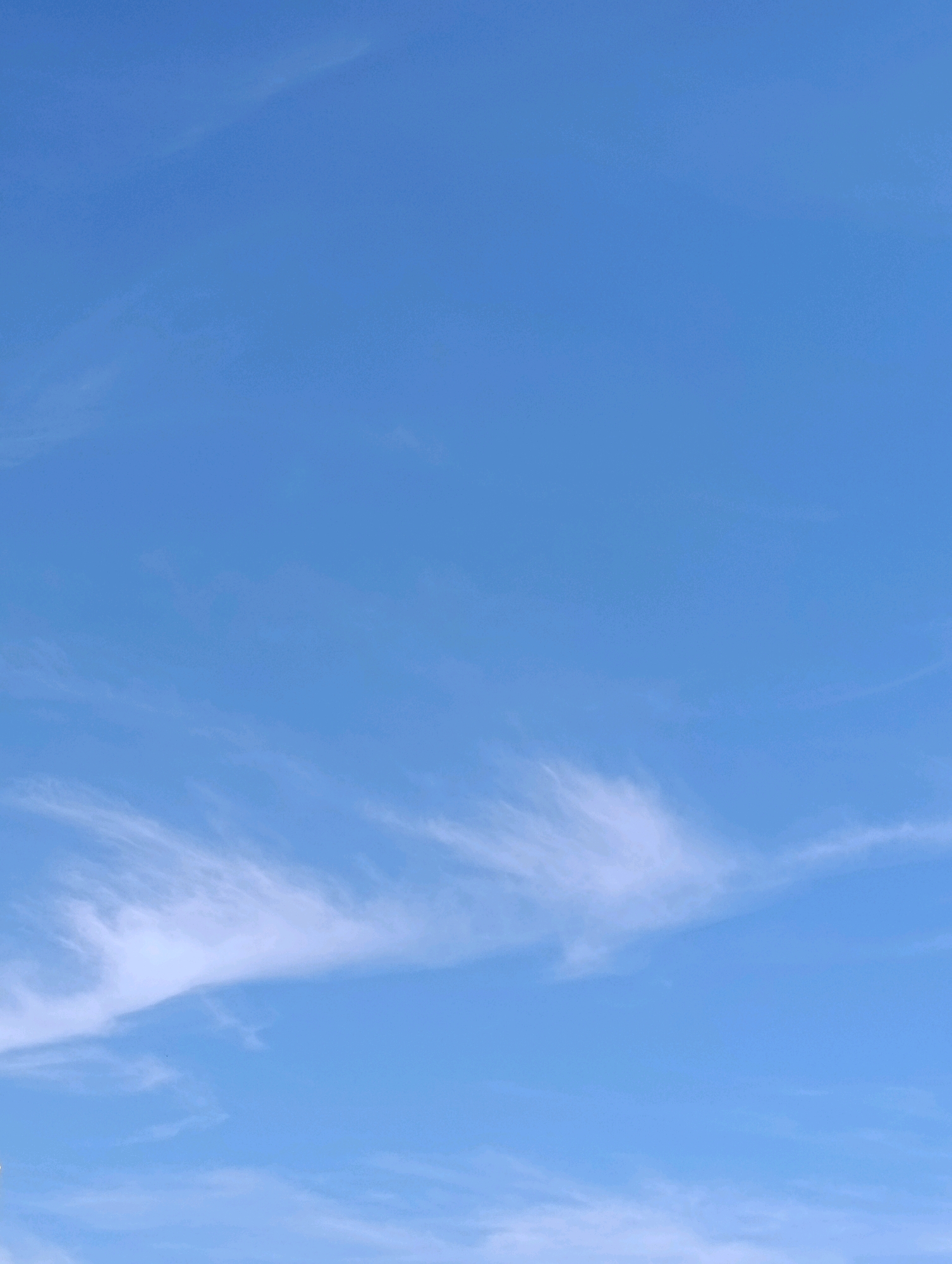 The image shows a clear blue sky with wispy white clouds. There are no people, subjects, objects, or actions visible. The scene is a vast expanse of sky, devoid of any specific landmarks that would indicate a particular location within Setúbal, Portugal. The focus is entirely on the atmospheric conditions.