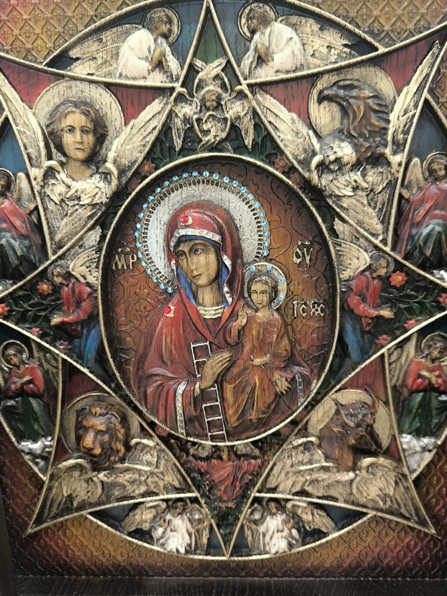 This image depicts a detailed icon, likely a religious artifact. At the center, Mary is shown holding the Christ child, rendered in a traditional Byzantine style with halos. Surrounding this central image are various symbolic figures, including what appear to be angels, a lion, and an eagle. The icon is ornate, with textured surfaces and gold-colored accents. The background features a patterned texture. There are no discernible clues within the image itself that indicate its location in Novosibirsk, Russia.