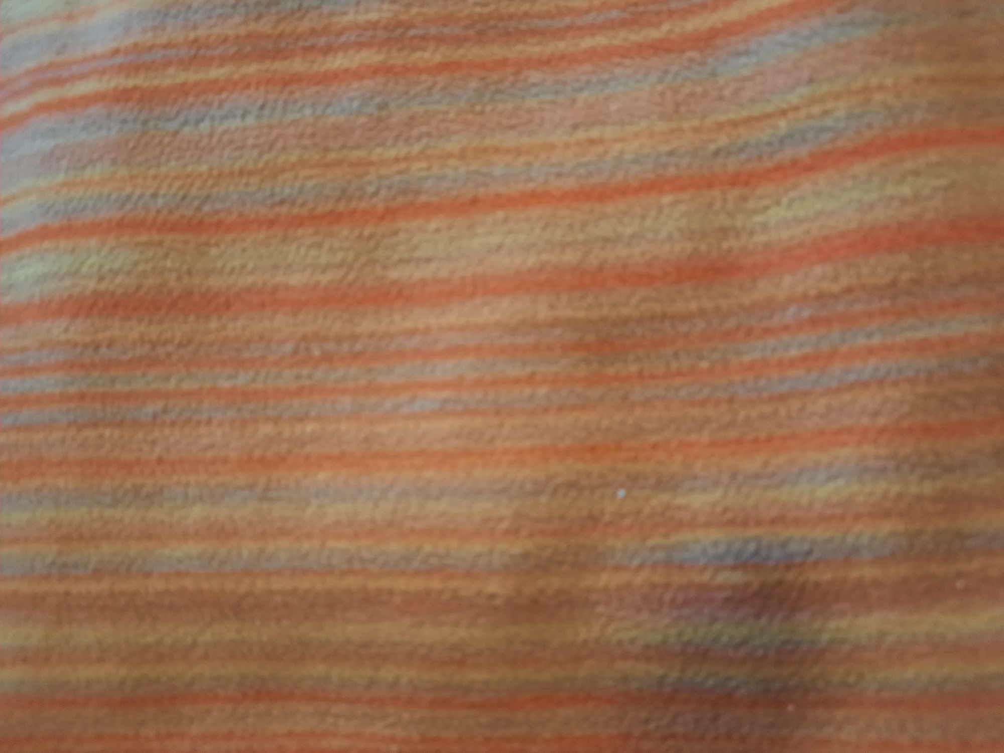 The image is a close-up, out-of-focus shot of a fabric with vertical stripes. The colors are predominantly shades of orange, yellow, and a muted blue or gray. The texture of the fabric appears to be woven, with fine vertical lines creating a ribbed or corded effect. There are no discernable objects, people, or actions visible in the image, and the background is simply the textured fabric itself. The location of this image in the city of Unknown, Unknown is not depicted or suggested by the visual content.