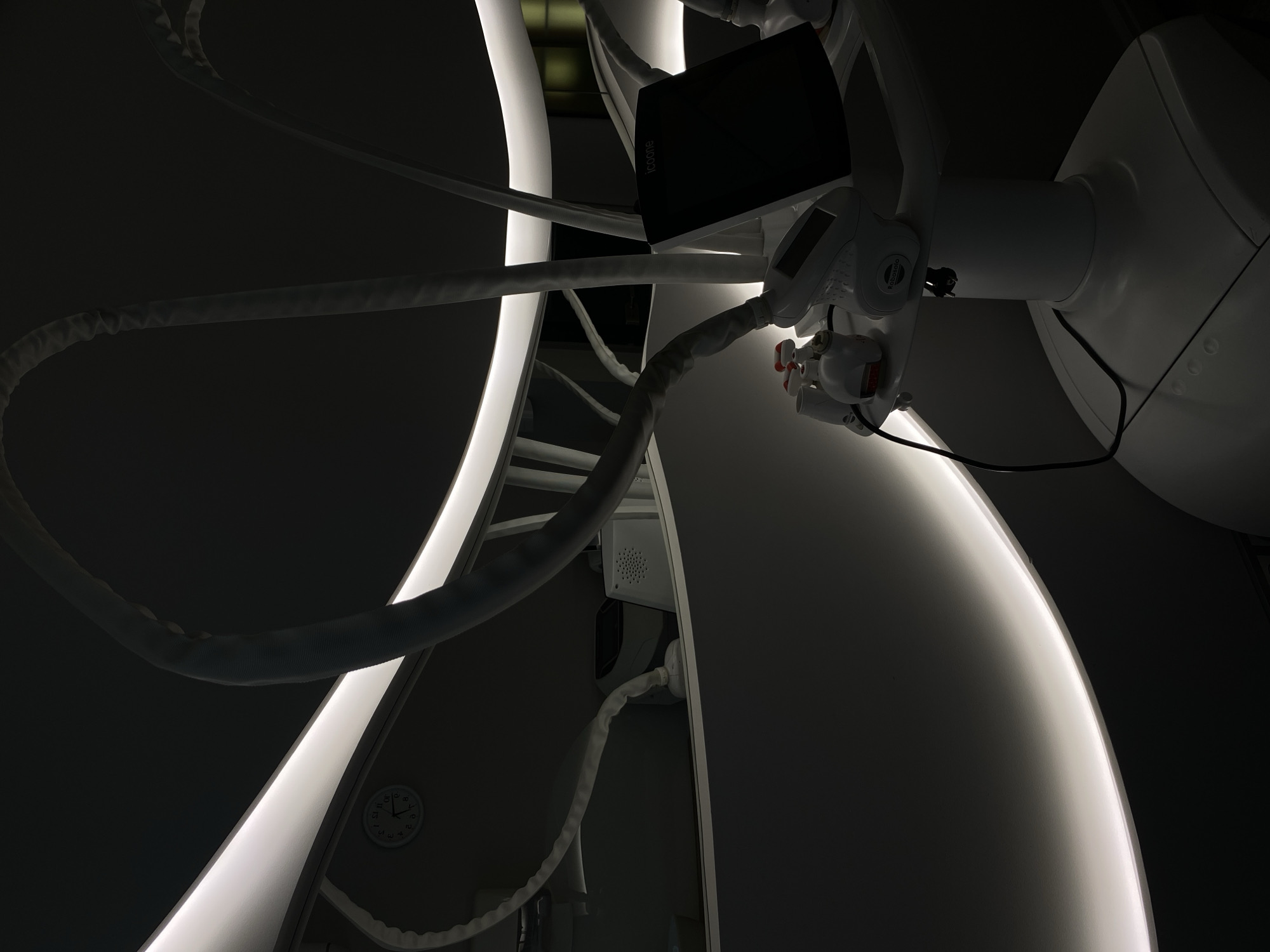 This image shows a close-up of a piece of medical equipment, likely a cosmetic treatment device, in a dimly lit room. The device is white and has several flexible tubes or hoses extending from it. A black screen or monitor is attached to the top of the device, displaying the logo "icoone". Below the screen are control buttons and other components. A circular clock is visible in the background, reflecting in a curved, illuminated surface. The overall impression is one of a modern, sterile environment. The location is specified as Votkinsk, Russia.